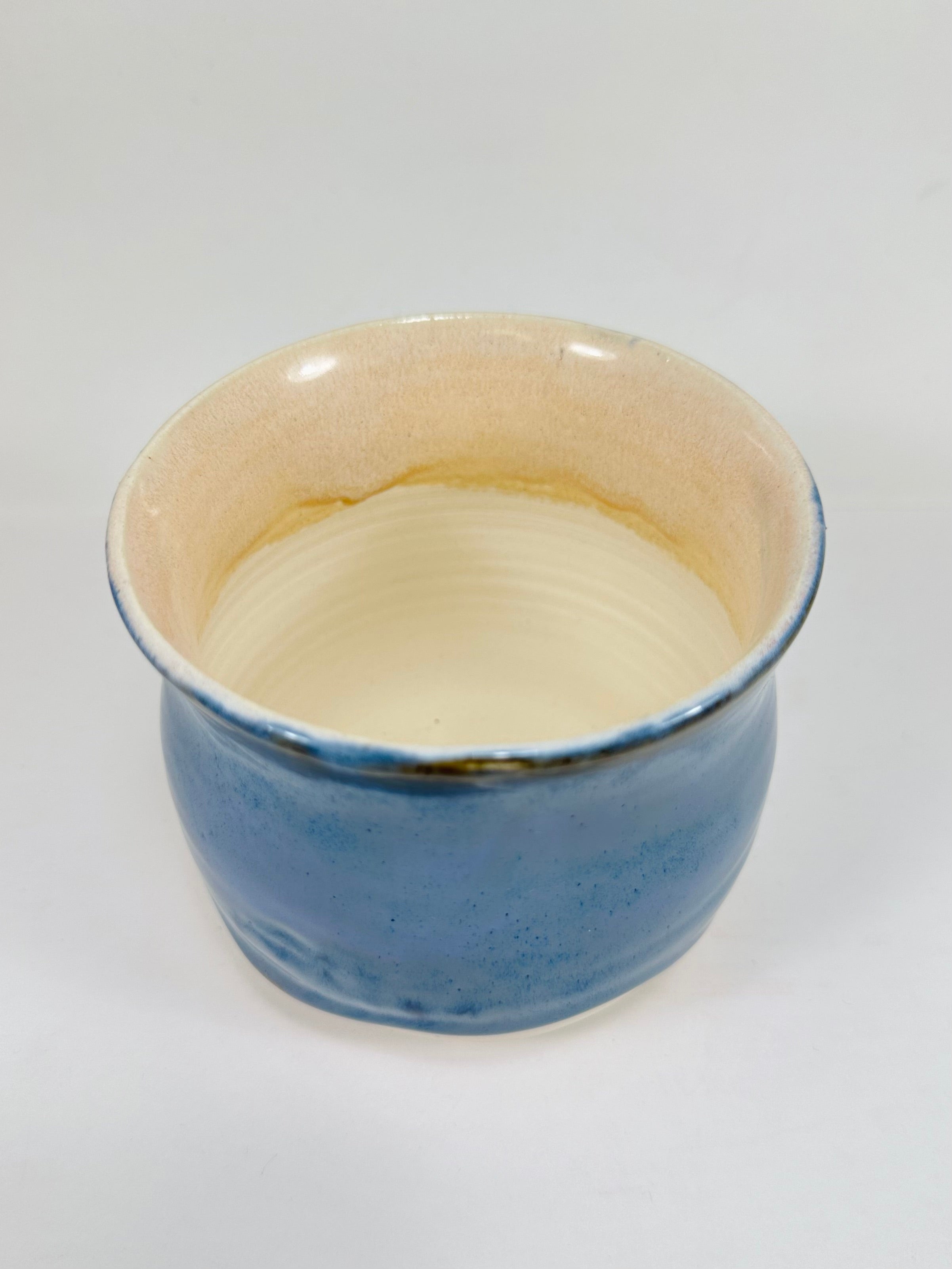 A handmade ceramic planter. The planter is glazed in a beautiful blue and cream colour. The planter is round in shape with a wide flared rim. The planter is left unglazed on the inside and on the bottom quarter of the pot.