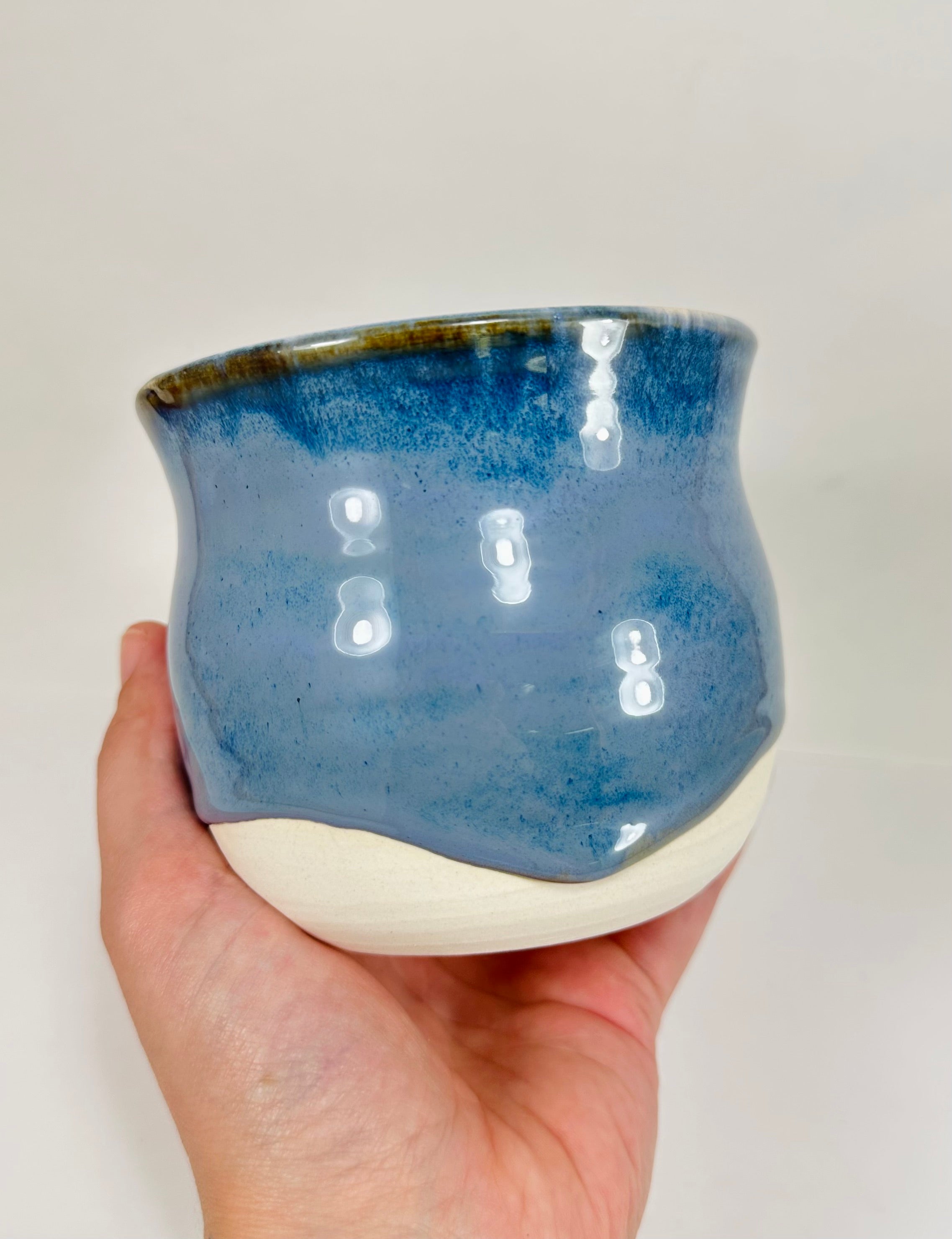 A handmade ceramic planter. The planter is glazed in a beautiful blue and cream colour. The planter is round in shape with a wide flared rim. The planter is left unglazed on the inside and on the bottom quarter of the pot.