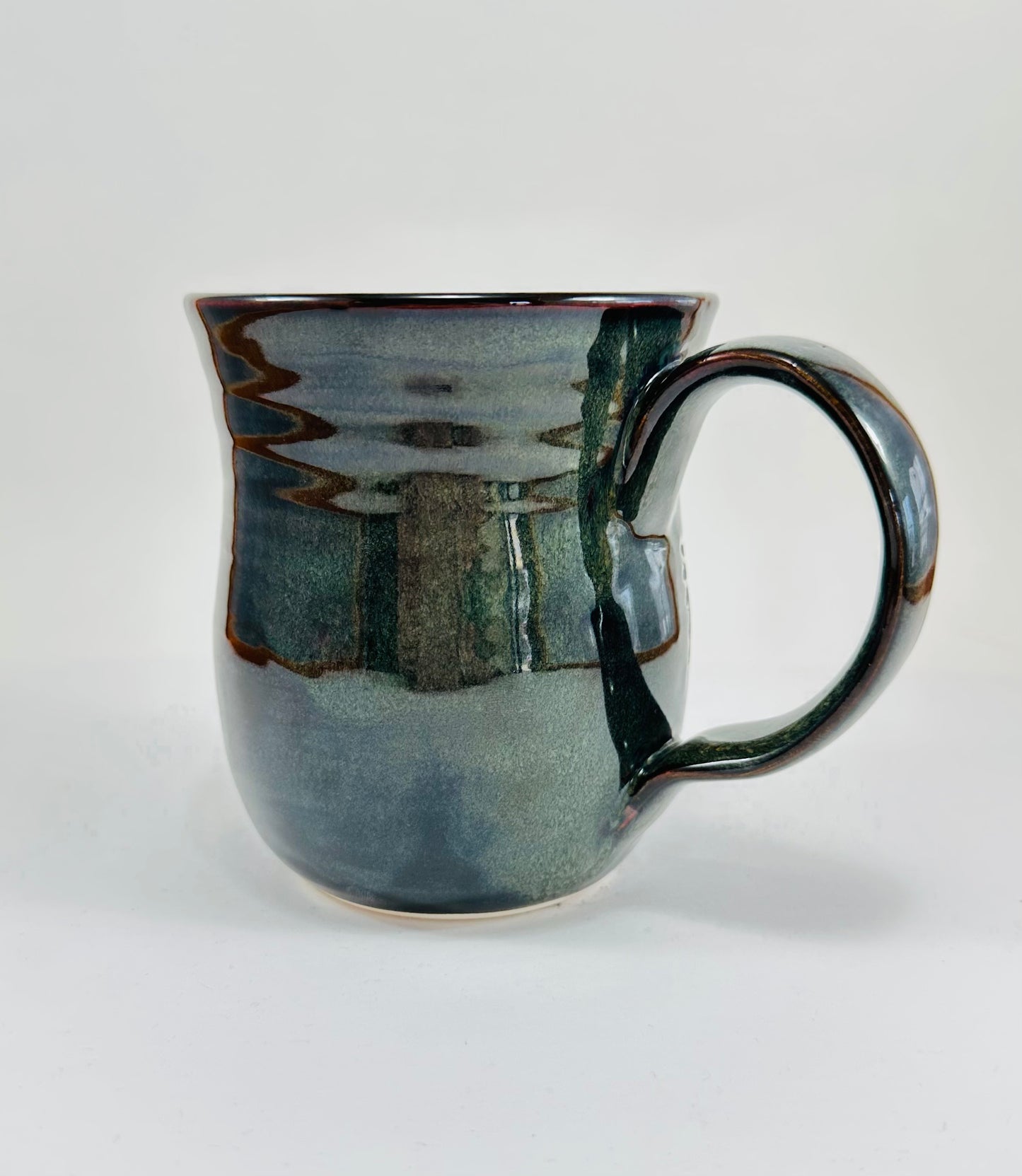 A handmade ceramic mug with an illustration of a wolf head and arrow on it. The mug is glazed in a beautiful dark blue/green glaze an has a smooth comfortable handle. The mug is made from porcelain clay.