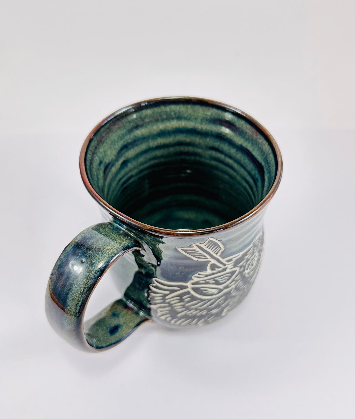 A handmade ceramic mug with an illustration of a wolf head and arrow on it. The mug is glazed in a beautiful dark blue/green glaze an has a smooth comfortable handle. The mug is made from porcelain clay.