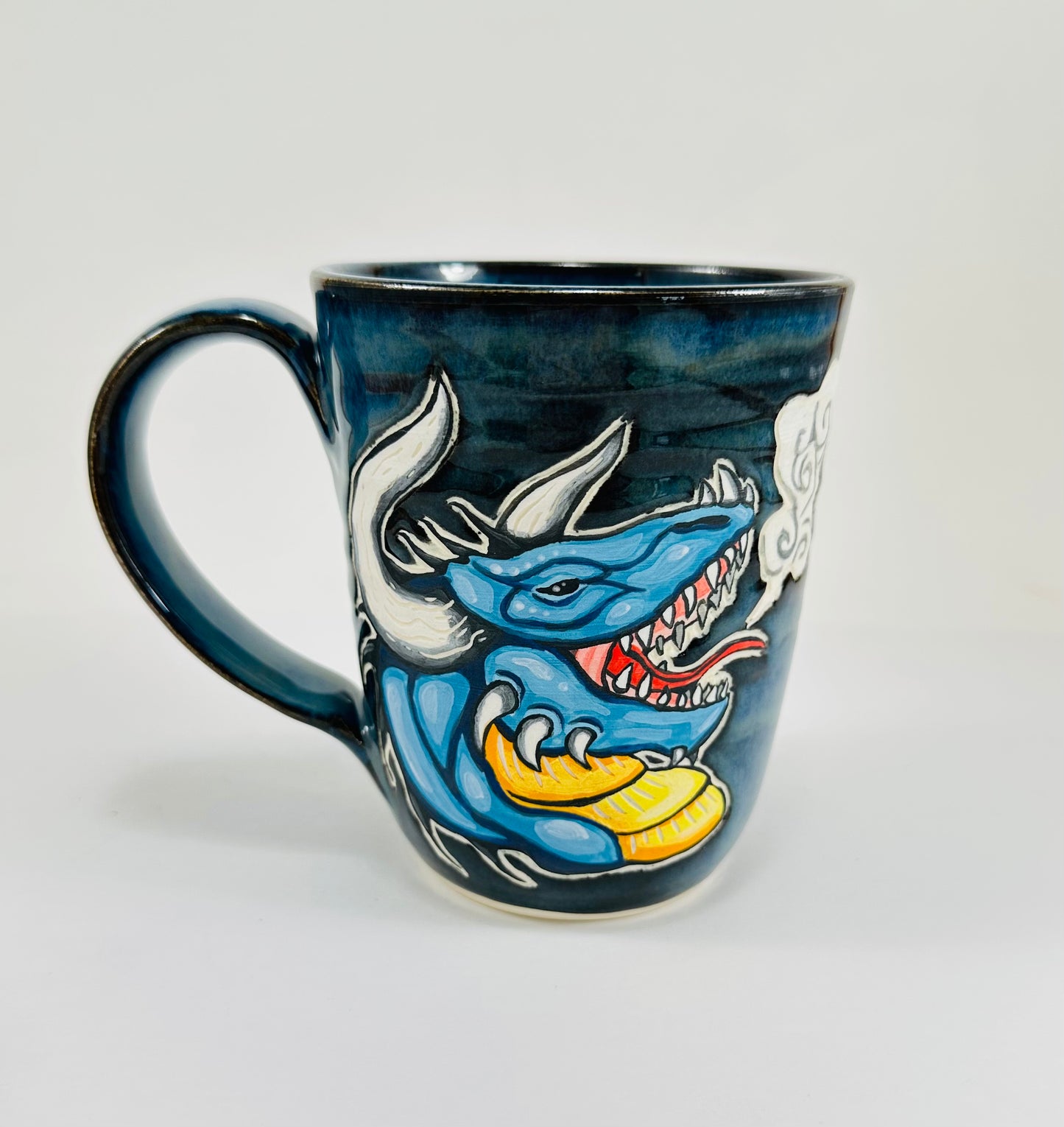 A handmade ceramic mug with a blue dragon illustration on it. The mug is glazed in a beautiful blue glaze and is made from porcelain clay.
