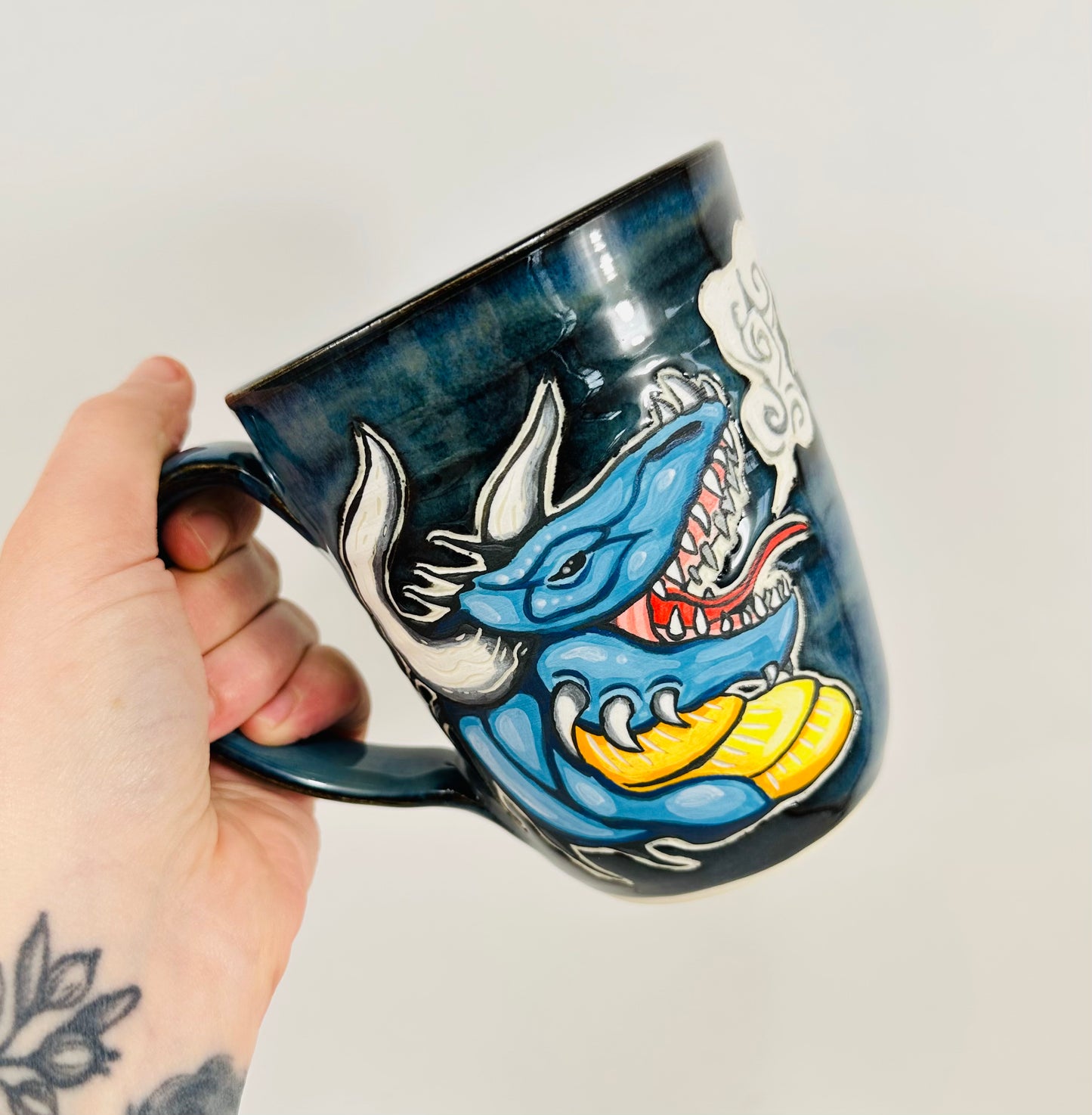 A handmade ceramic mug with a blue dragon illustration on it. The mug is glazed in a beautiful blue glaze and is made from porcelain clay.