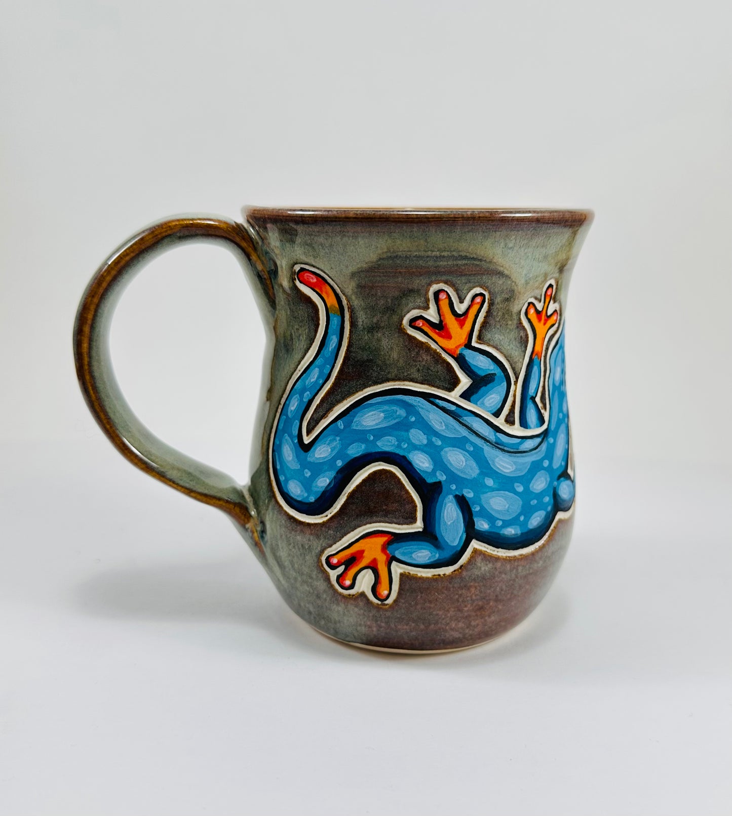 A handmade ceramic mug with a blue lizard illustration on it. The mug is made from porcelain clay and is glazed in a beautiful green glaze.