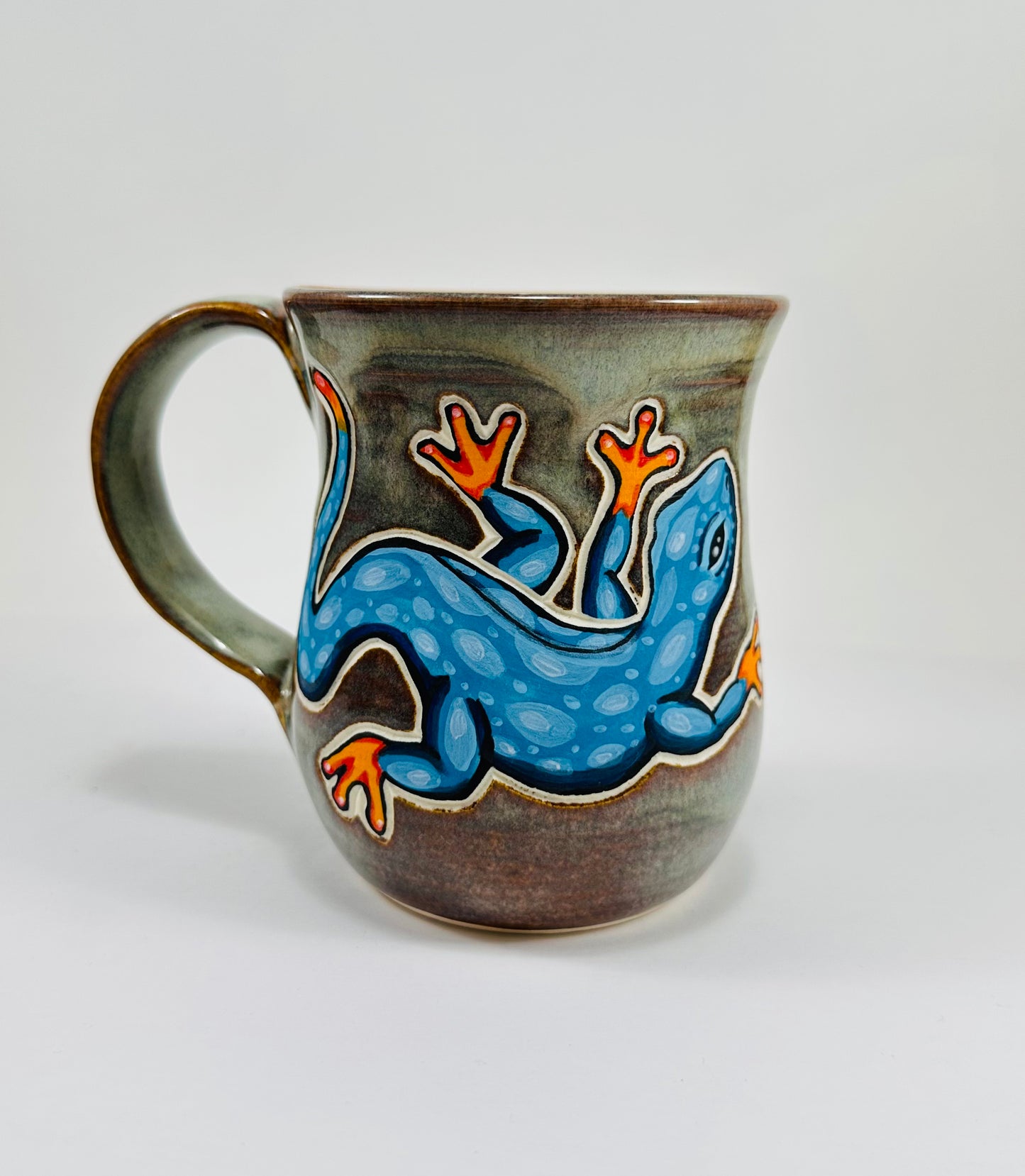 A handmade ceramic mug with a blue lizard illustration on it. The mug is made from porcelain clay and is glazed in a beautiful green glaze.