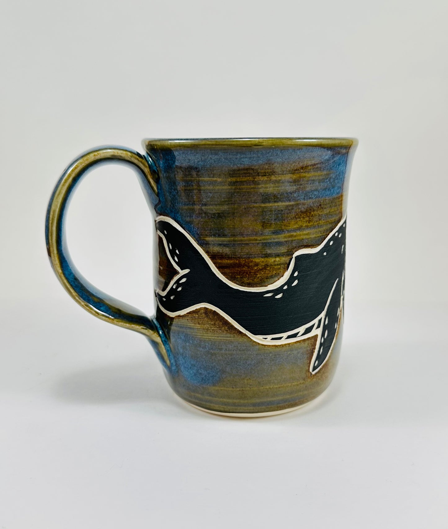 A handmade ceramic mug with a blue whale illustration on it and fish. The mug is made from porcelain clay and has a beautiful blue and brown glaze.