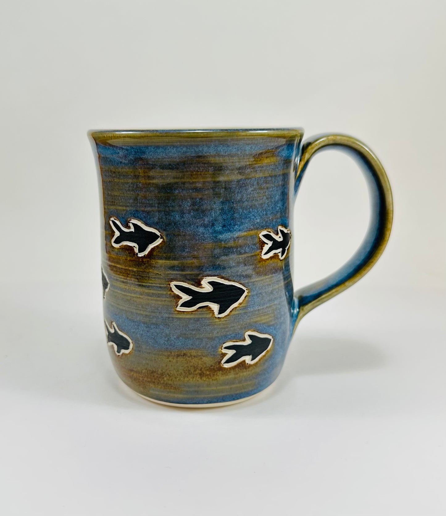 A handmade ceramic mug with a blue whale illustration on it and fish. The mug is made from porcelain clay and has a beautiful blue and brown glaze.
