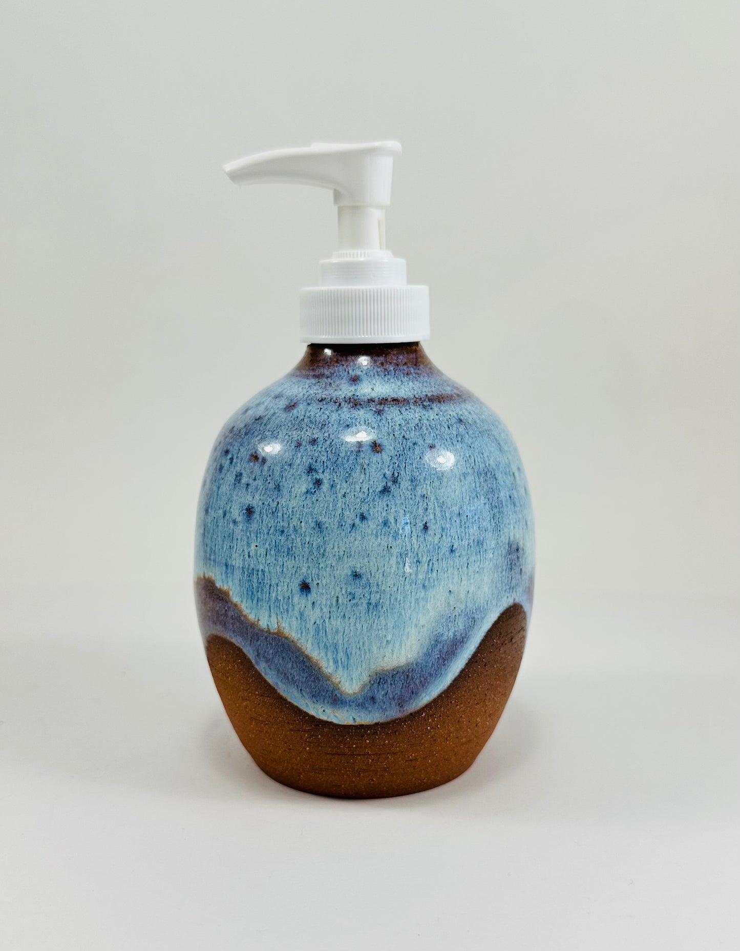 A handmade ceramic soap dispenser in red clay with a beautiful blue glaze.