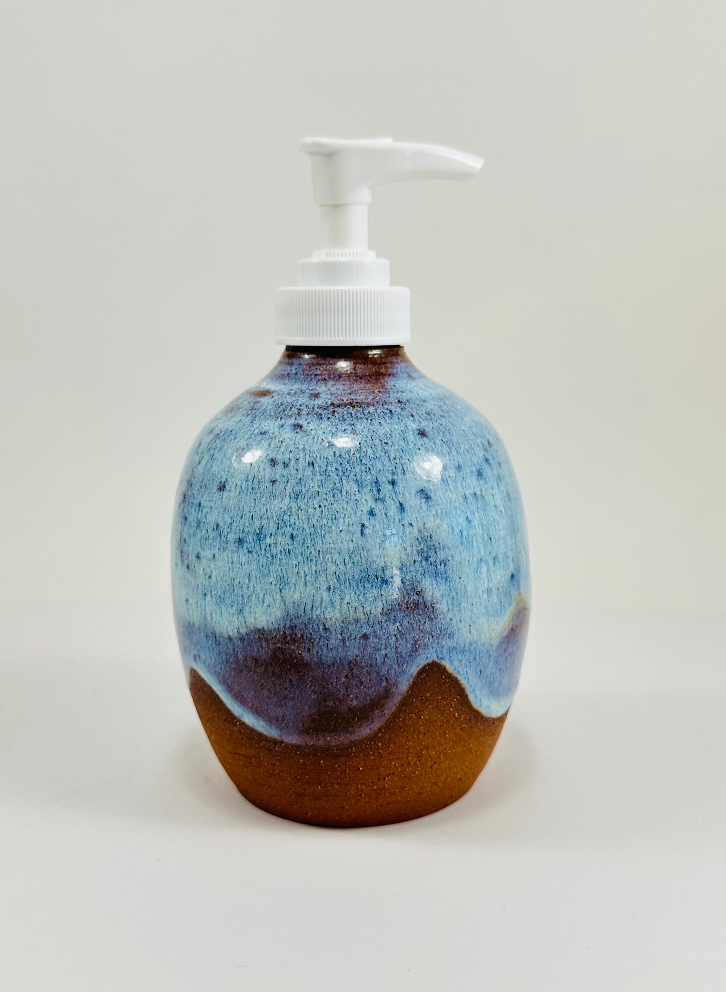 A handmade ceramic soap dispenser in red clay with a beautiful blue glaze.