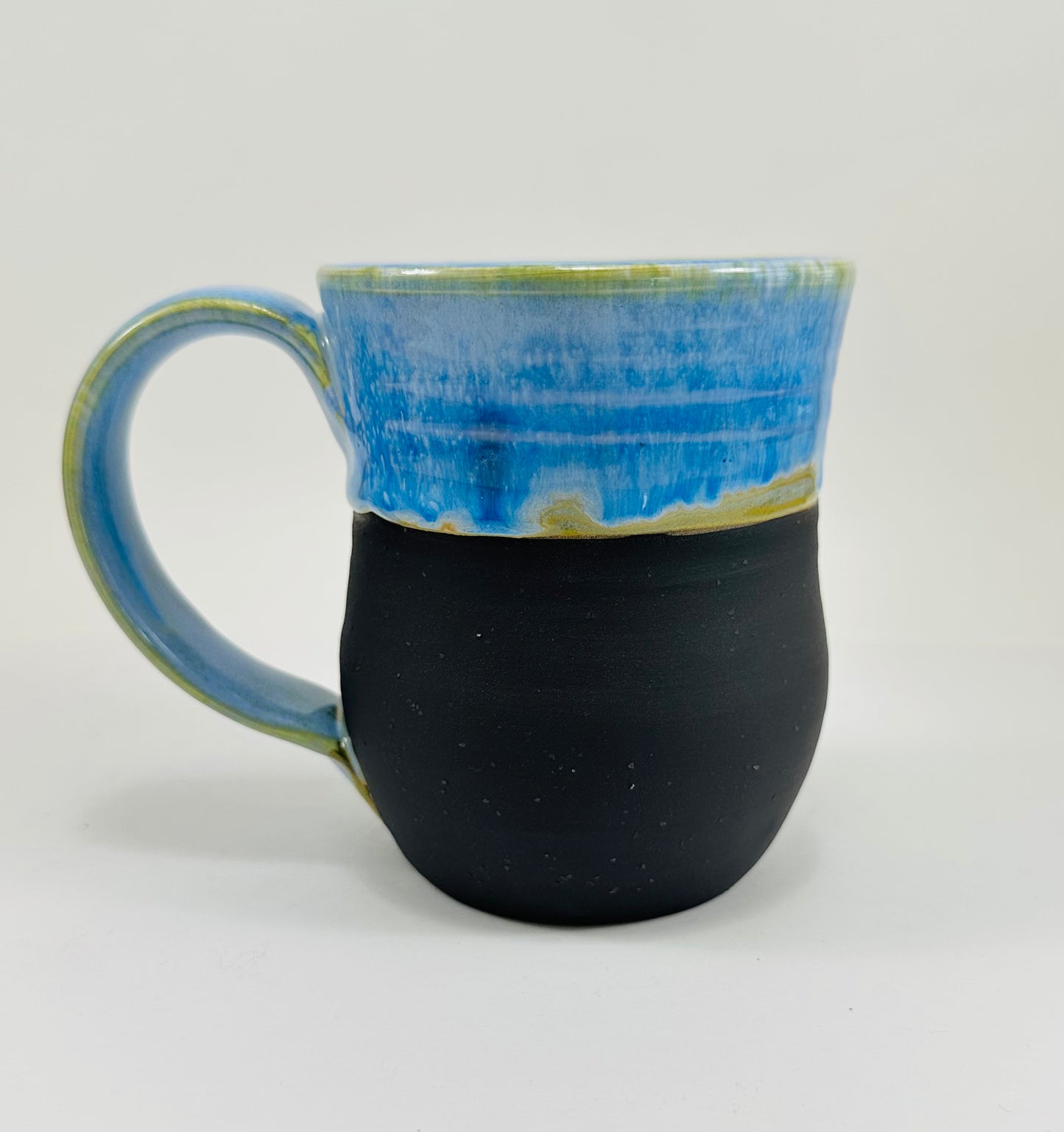 A handmade ceramic mug with a beautiful blue glaze over a black base. The mug is made from porcelain clay.