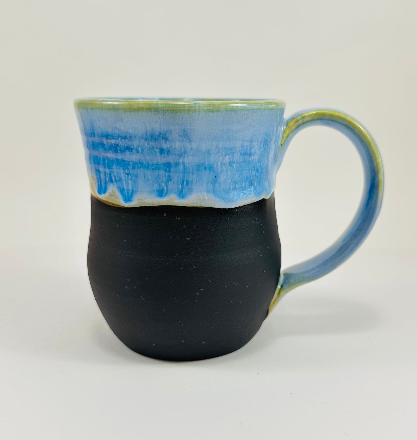 A handmade ceramic mug with a beautiful blue glaze over a black base. The mug is made from porcelain clay.