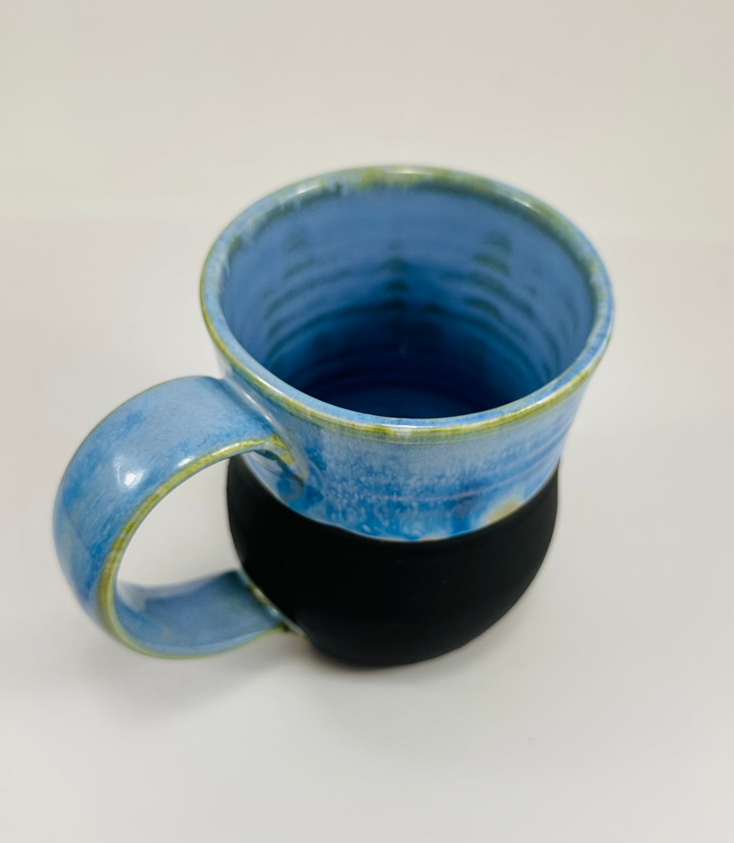 A handmade ceramic mug with a beautiful blue glaze over a black base. The mug is made from porcelain clay.