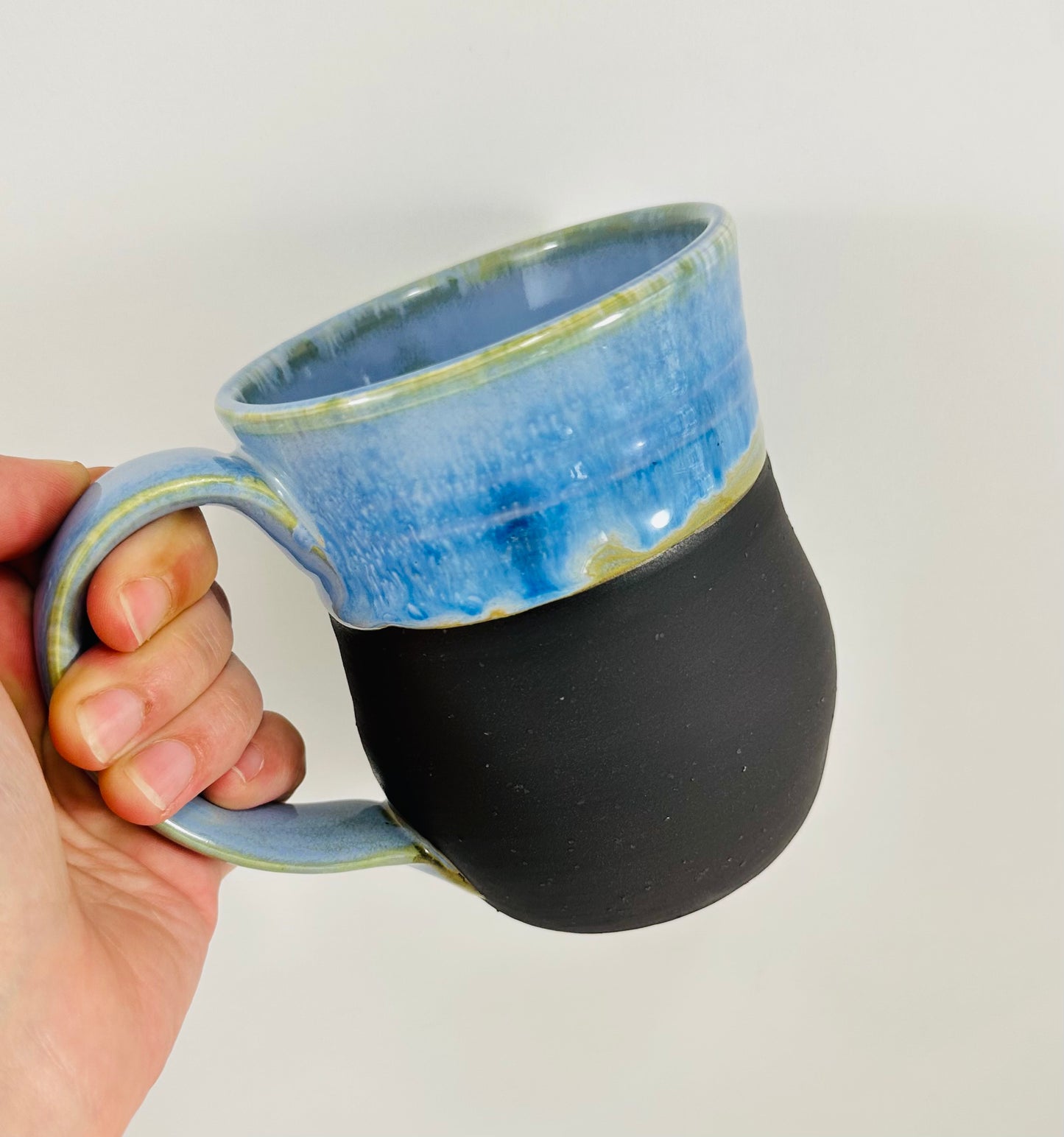 A handmade ceramic mug with a beautiful blue glaze over a black base. The mug is made from porcelain clay.