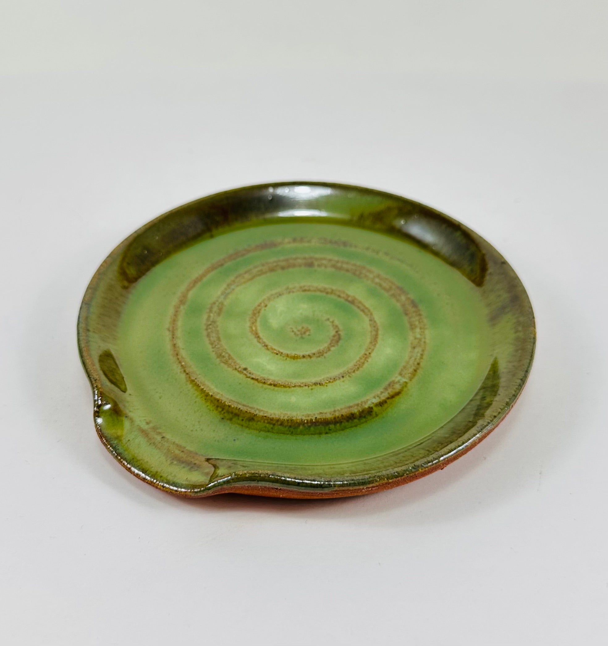 A handmade ceramic spoon rest in a beautiful green glaze on red clay.