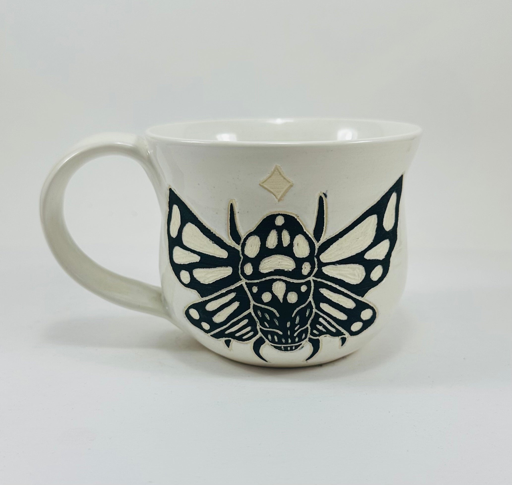 A handmade ceramic mug in a beautiful white glaze with a cicada illustration on it.