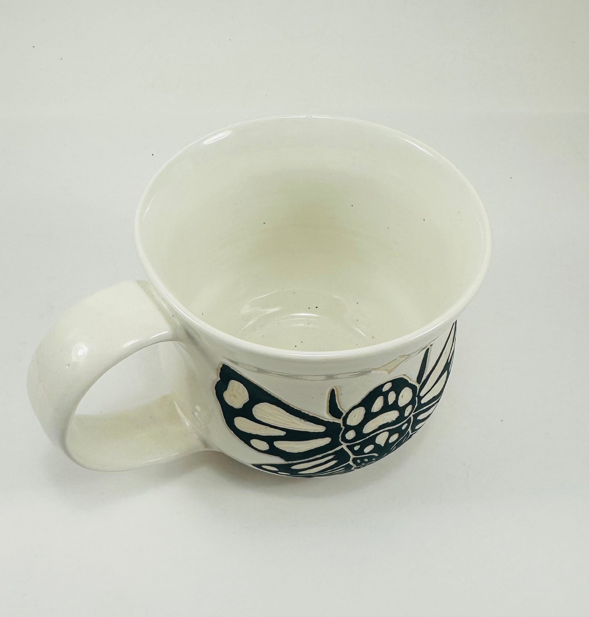 A handmade ceramic mug in a beautiful white glaze with a cicada illustration on it.