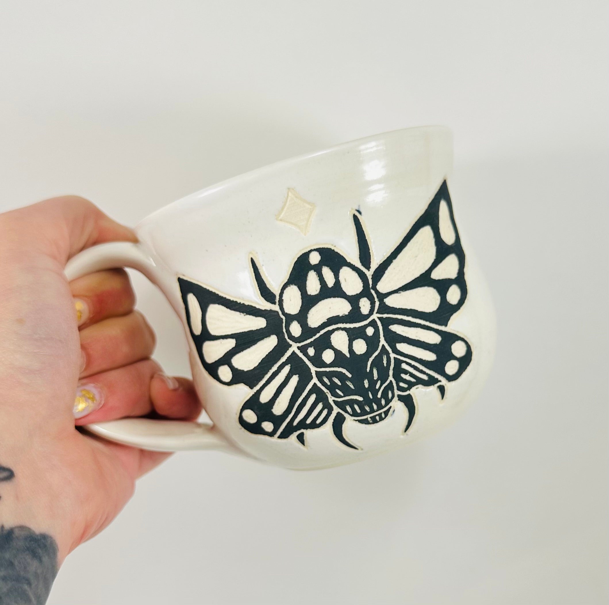 A handmade ceramic mug in a beautiful white glaze with a cicada illustration on it.