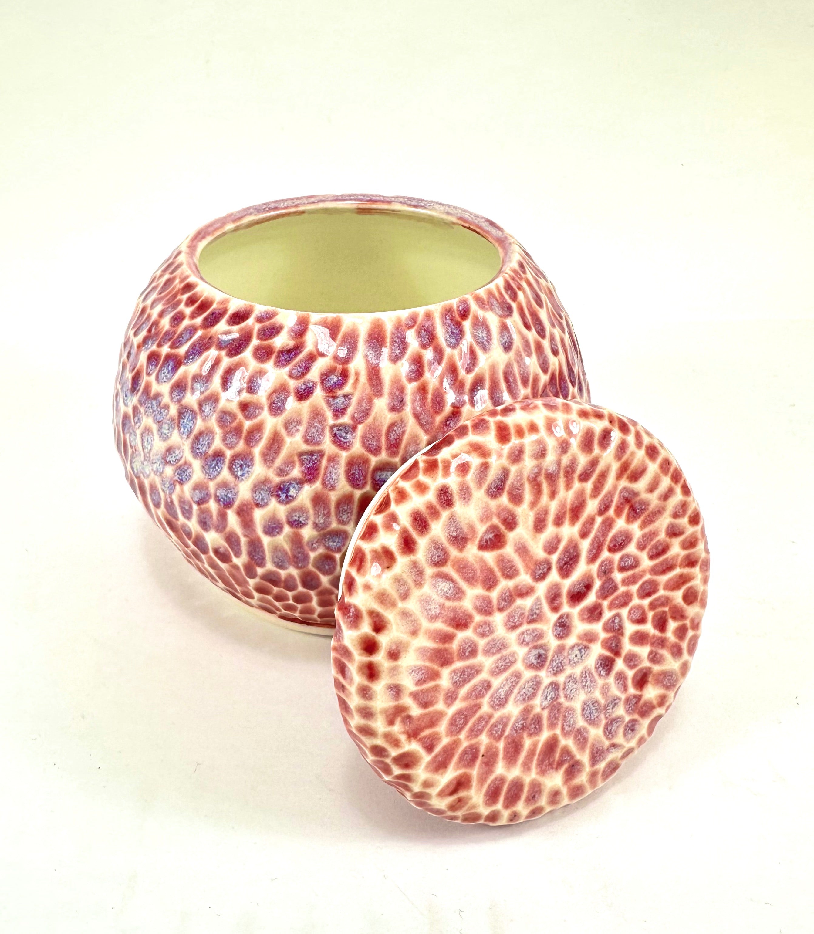 A handmade ceramic sugar jar, The sugar jar is glazed in a beautiful pink, blue, beige and red glaze. It is carved all over to add texture. The sugar jar is round with a flat lid.