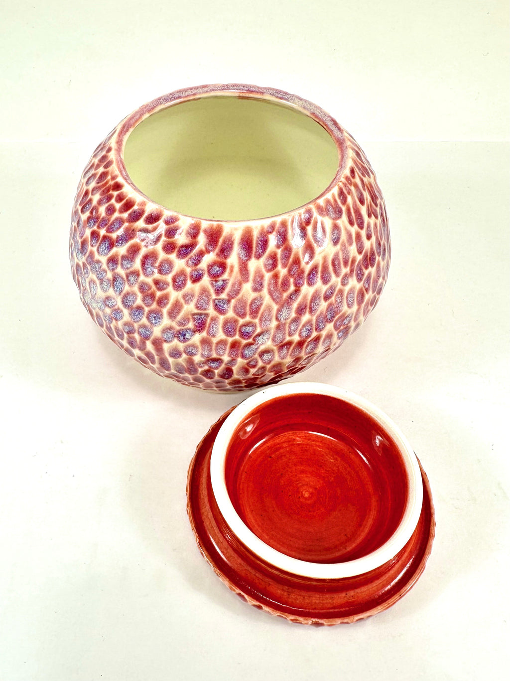 A handmade ceramic sugar jar, The sugar jar is glazed in a beautiful pink, blue, beige and red glaze. It is carved all over to add texture. The sugar jar is round with a flat lid.