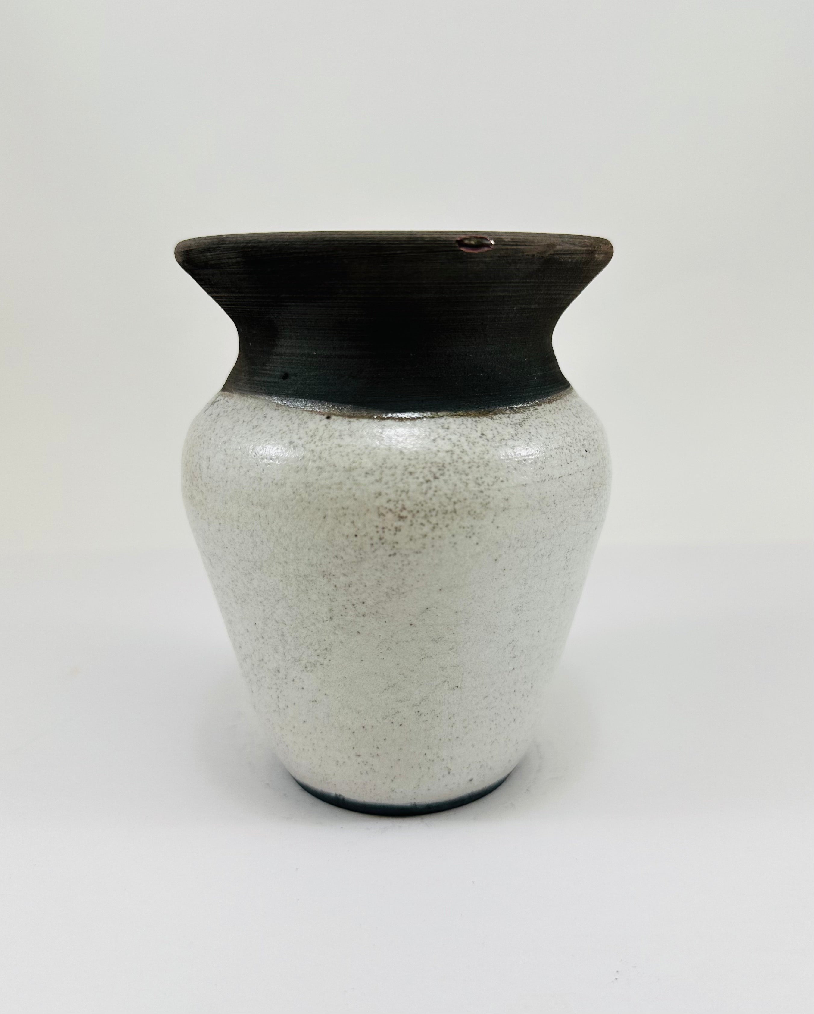 A hand made ceramic vase with a stunning, matte Raku glaze. The colours show whites and blacks. The vase has a V shaped body, narrow neck and wide opening. The top third of the pot is black and the bottom two thirds is white.