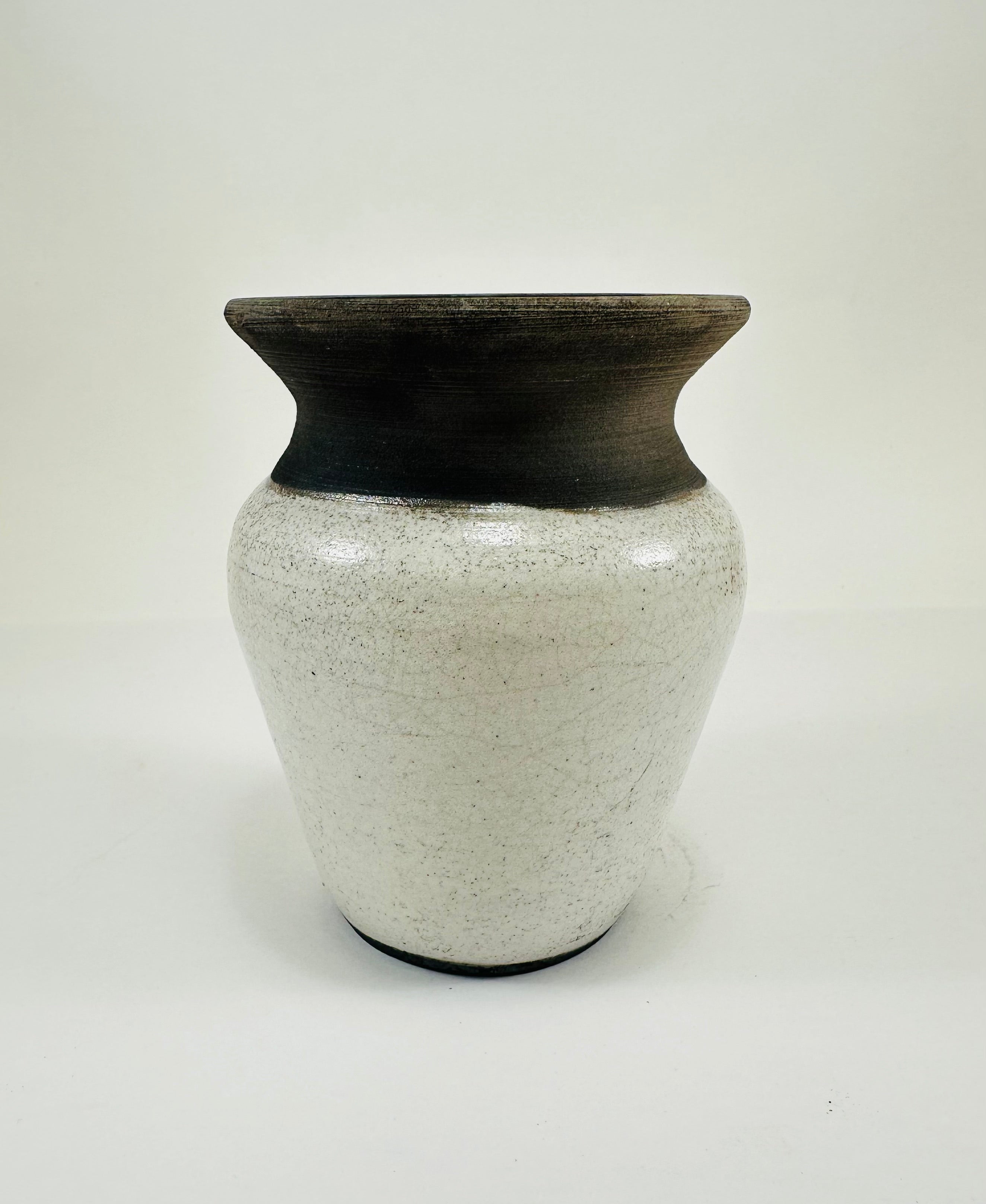 A hand made ceramic vase with a stunning, matte Raku glaze. The colours show whites and blacks. The vase has a V shaped body, narrow neck and wide opening. The top third of the pot is black and the bottom two thirds is white.