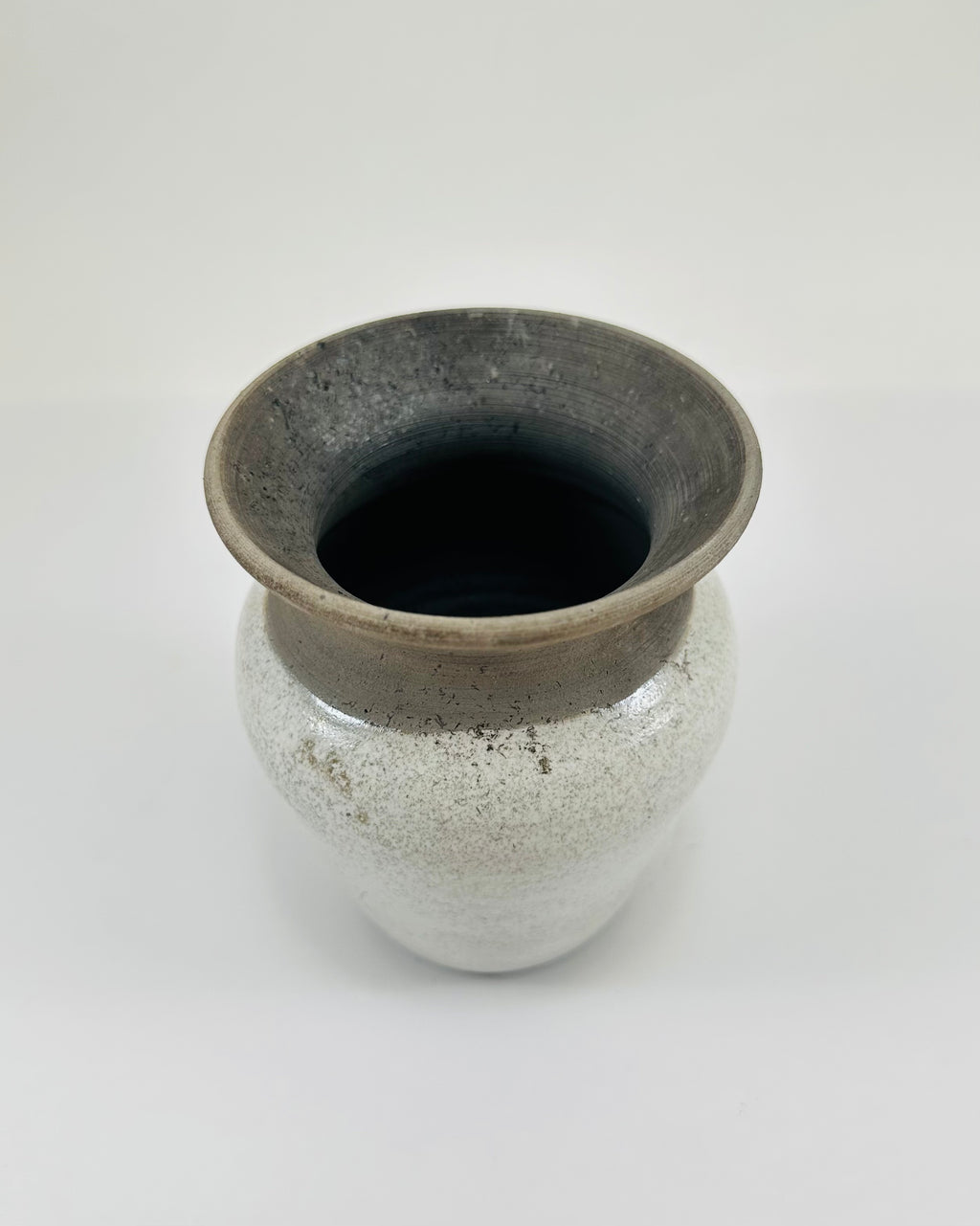 A hand made ceramic vase with a stunning, matte Raku glaze. The colours show whites and blacks. The vase has a V shaped body, narrow neck and wide opening. The top third of the pot is black and the bottom two thirds is white.
