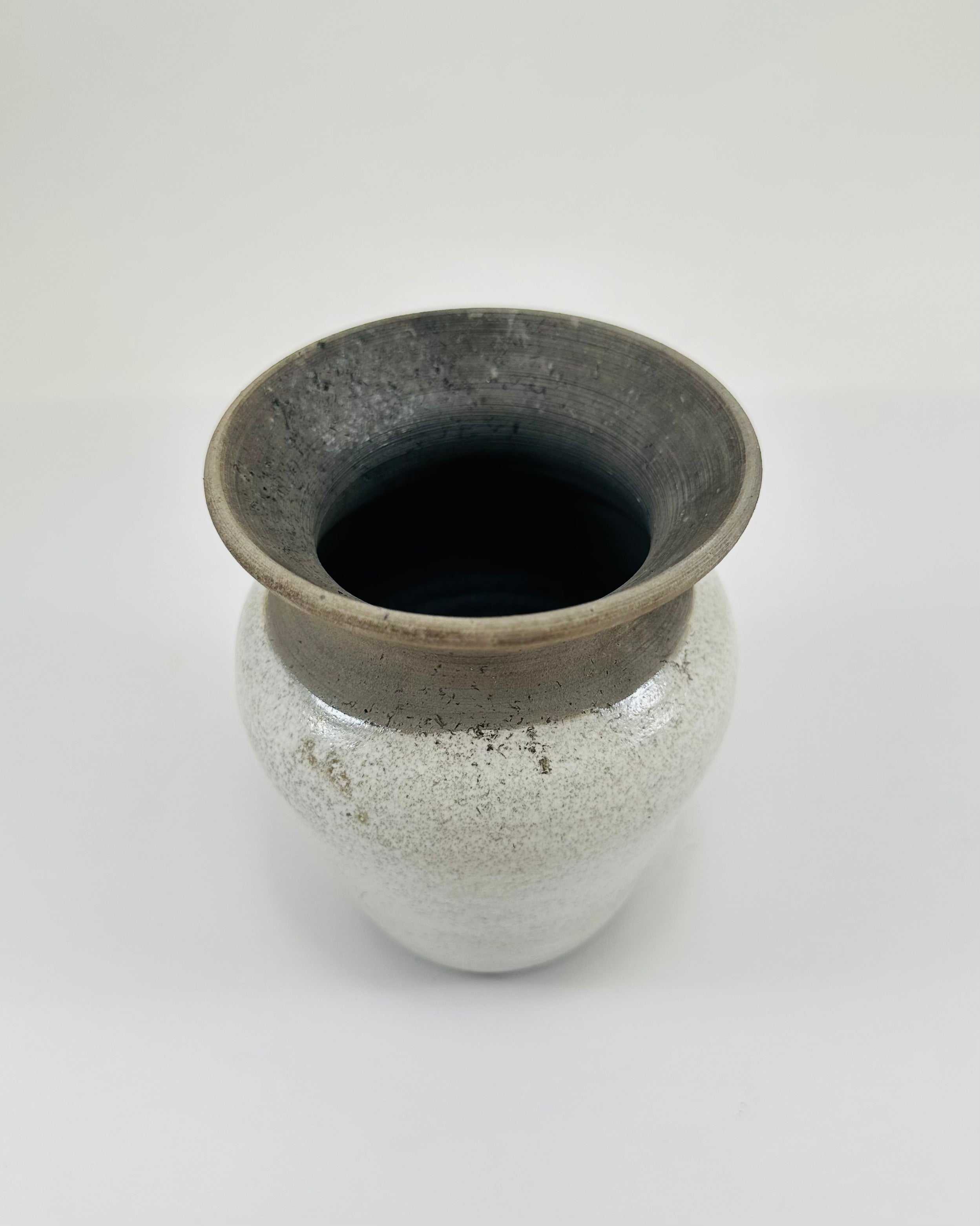 A hand made ceramic vase with a stunning, matte Raku glaze. The colours show whites and blacks. The vase has a V shaped body, narrow neck and wide opening. The top third of the pot is black and the bottom two thirds is white.
