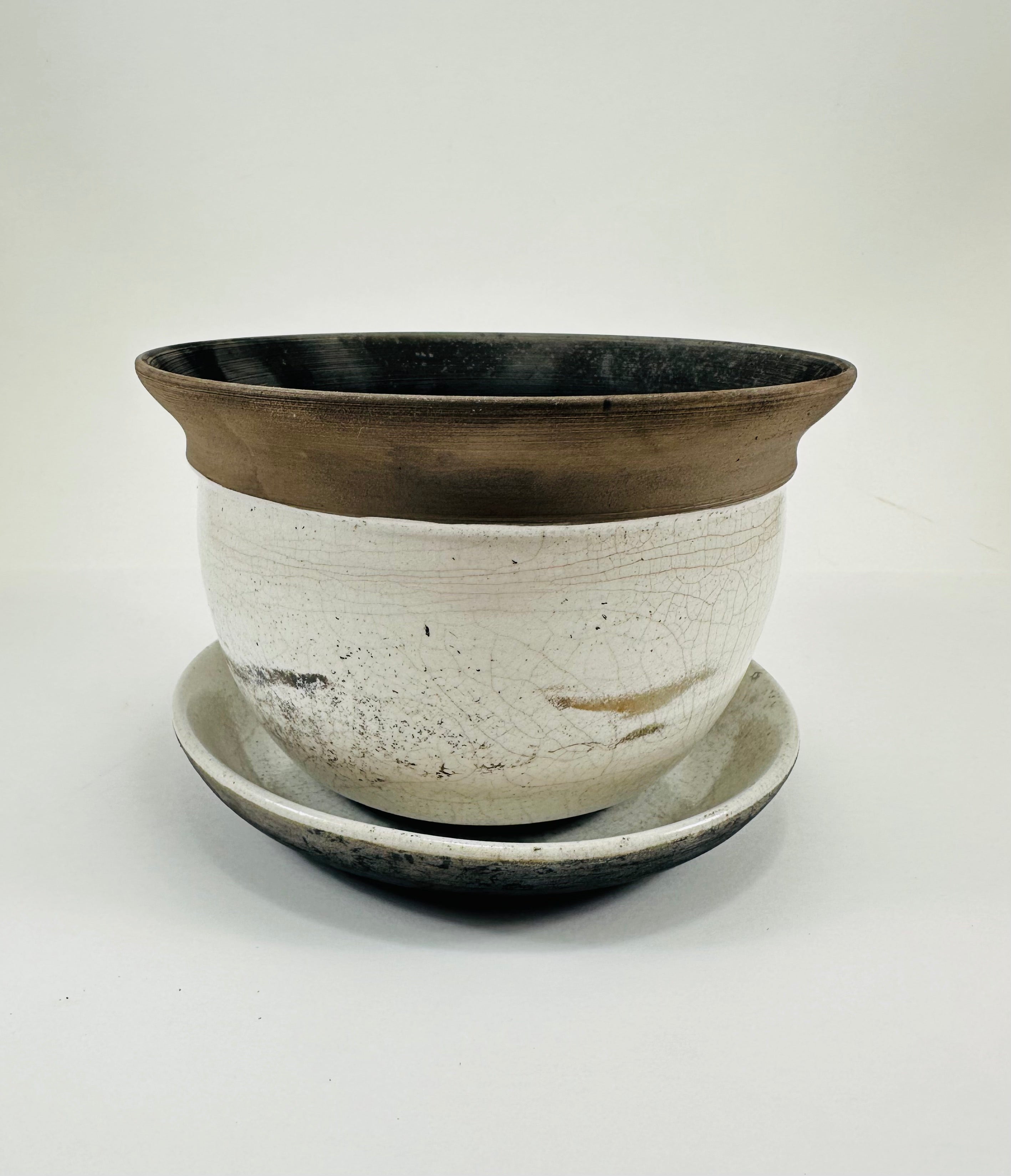 A hand made ceramic planter and plate with a stunning, matte Raku glaze. The colours show whites and blacks. The planter is bowl shaped and has a flared opening. The top rim of the planter is black and the bottom body and plate is white.