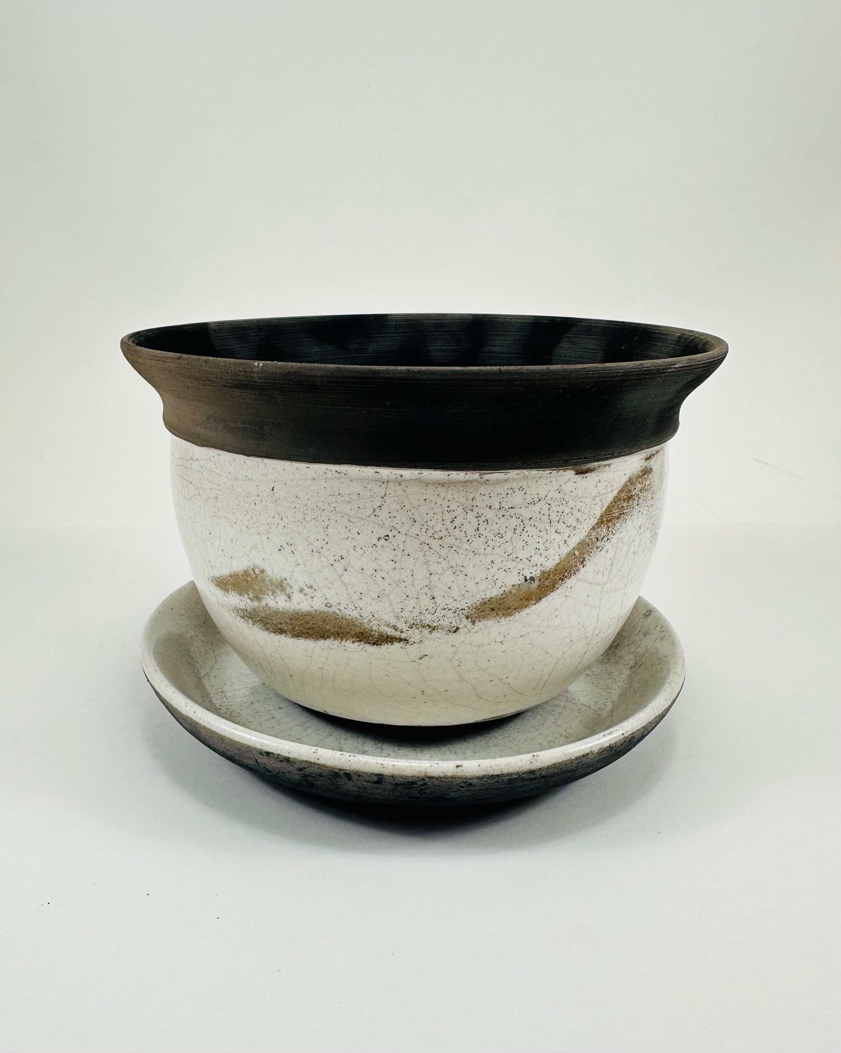 A hand made ceramic planter and plate with a stunning, matte Raku glaze. The colours show whites and blacks. The planter is bowl shaped and has a flared opening. The top rim of the planter is black and the bottom body and plate is white.