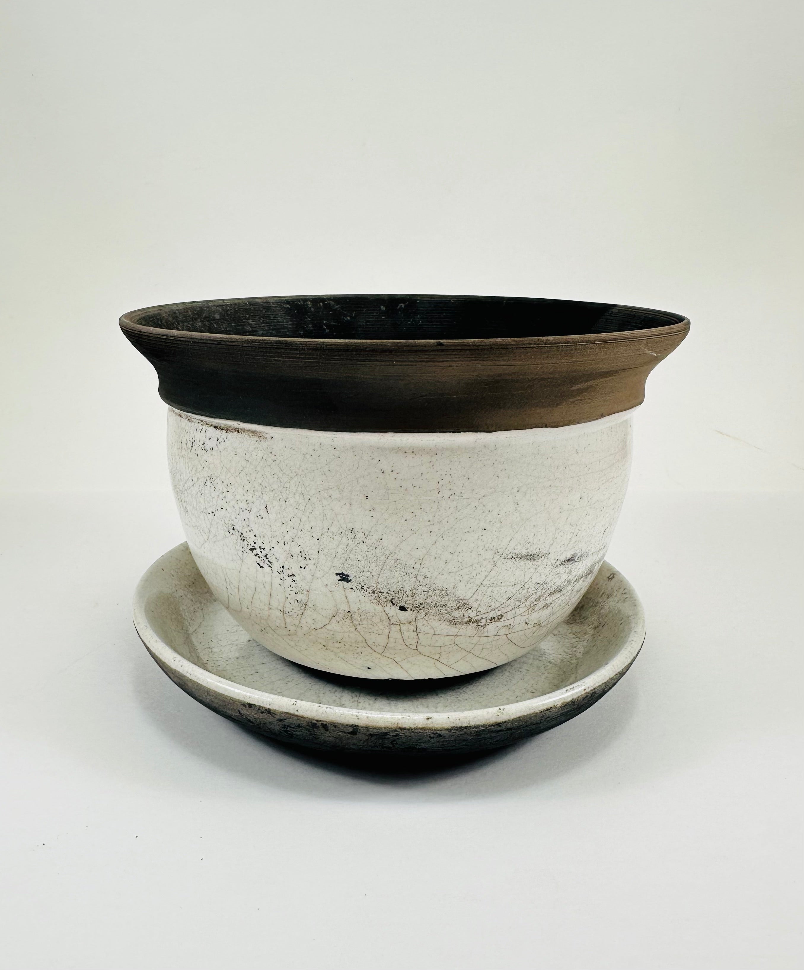 A hand made ceramic planter and plate with a stunning, matte Raku glaze. The colours show whites and blacks. The planter is bowl shaped and has a flared opening. The top rim of the planter is black and the bottom body and plate is white.