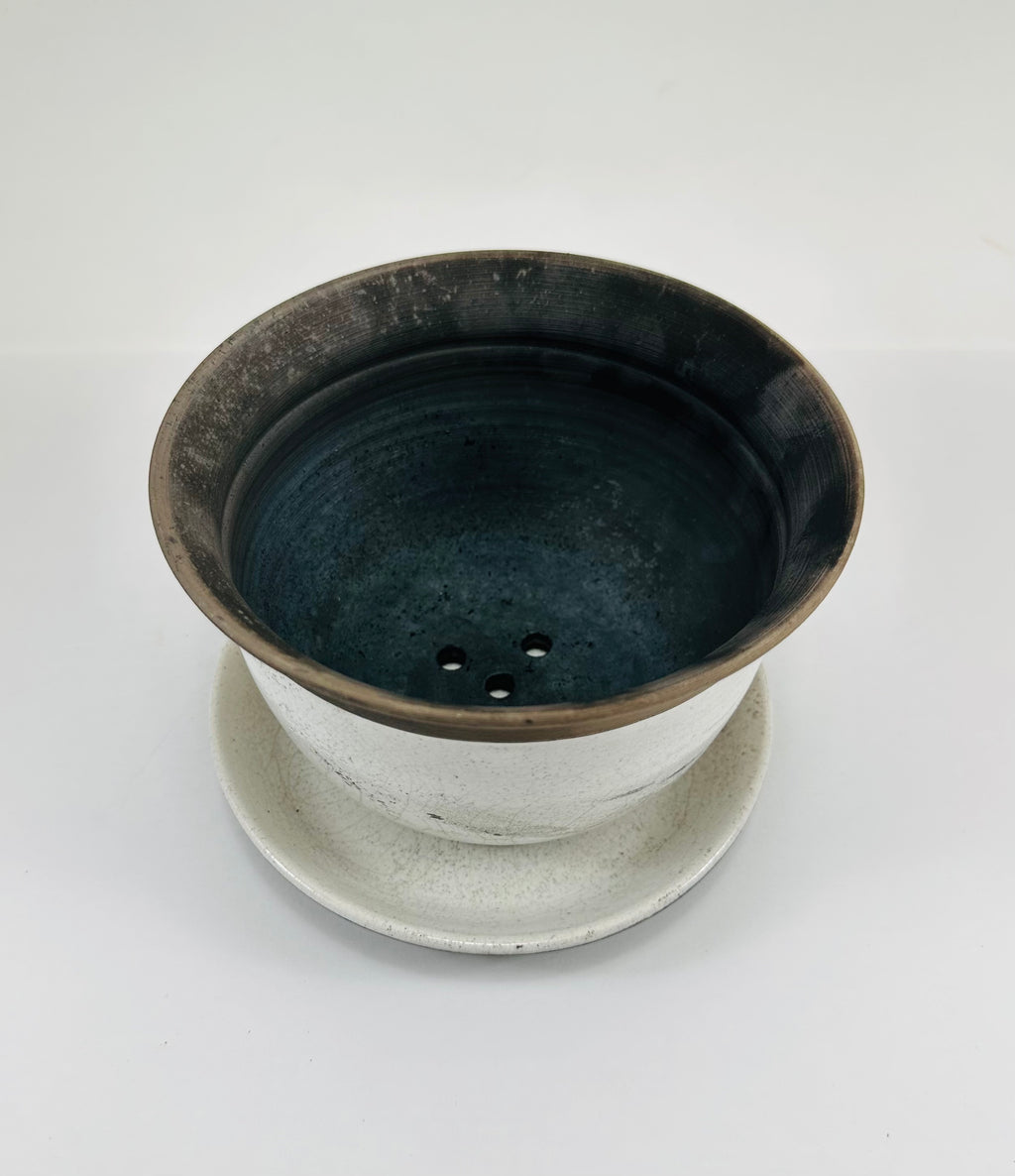 A hand made ceramic planter and plate with a stunning, matte Raku glaze. The colours show whites and blacks. The planter is bowl shaped and has a flared opening. The top rim of the planter is black and the bottom body and plate is white.