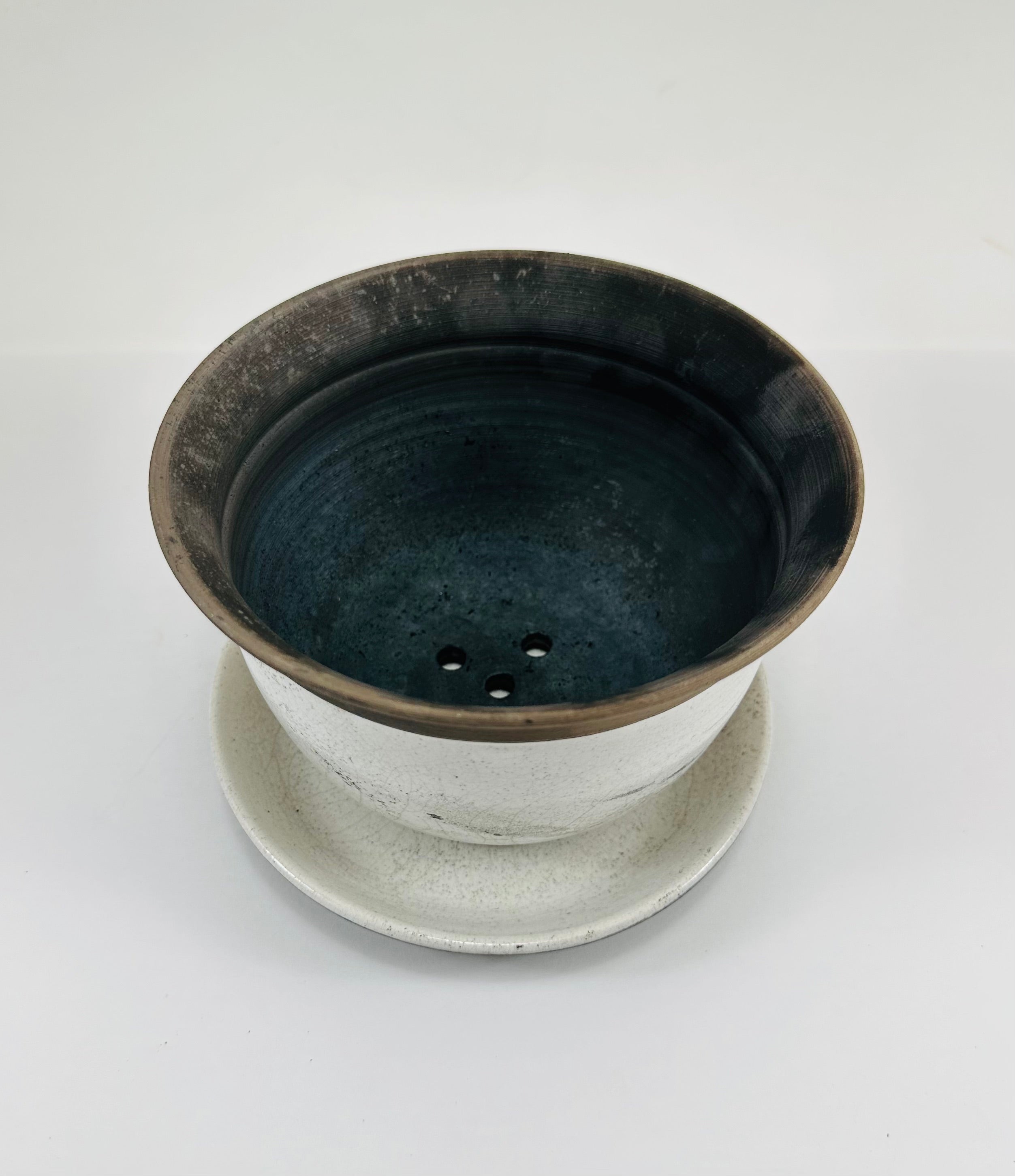 A hand made ceramic planter and plate with a stunning, matte Raku glaze. The colours show whites and blacks. The planter is bowl shaped and has a flared opening. The top rim of the planter is black and the bottom body and plate is white.