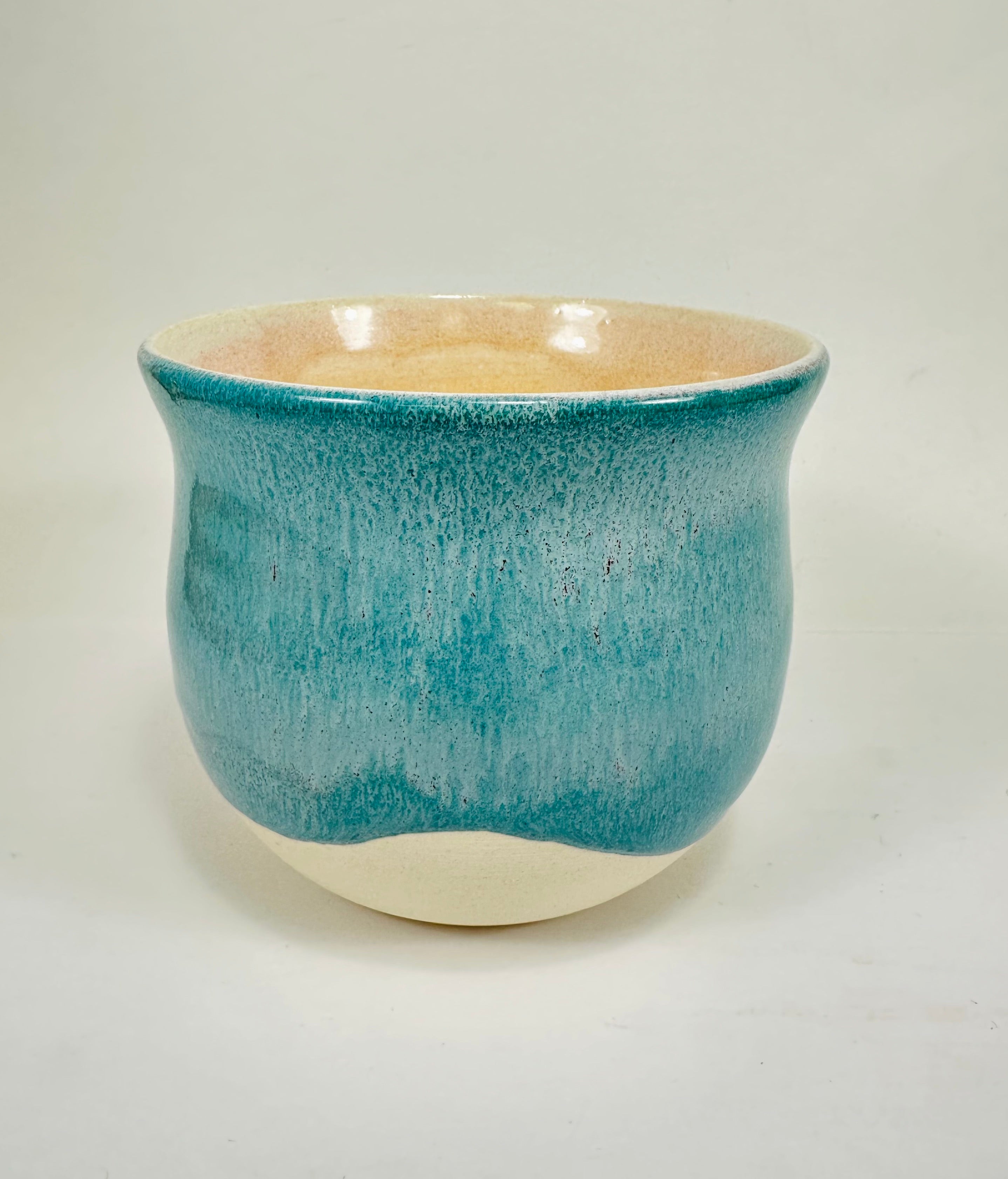 A handmade ceramic planter. The planter is glazed in a beautiful turquoise and cream colour. The planter is round in shape with a wide flared rim. The planter is left unglazed on the inside and on the bottom quarter of the pot.