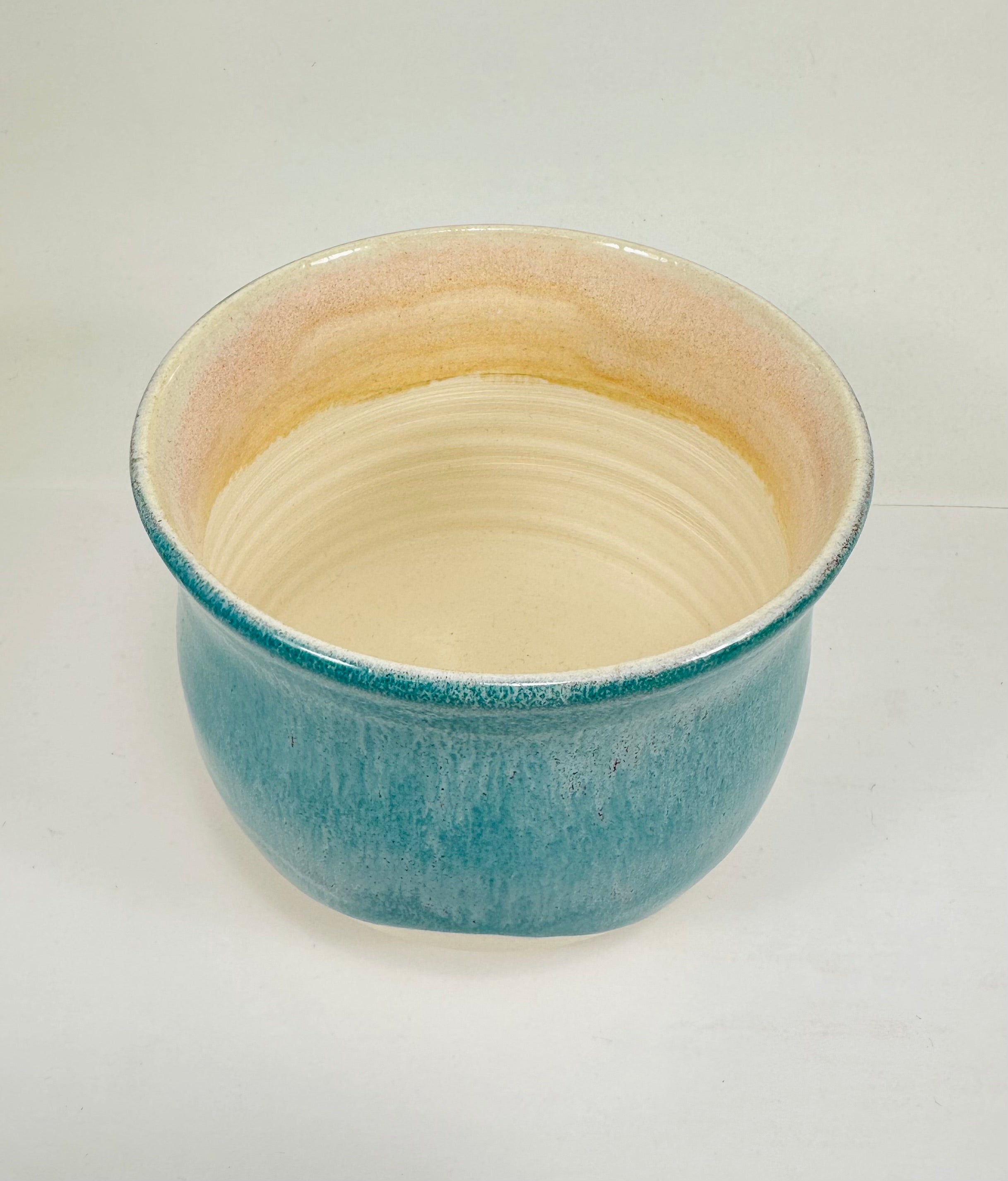 A handmade ceramic planter. The planter is glazed in a beautiful turquoise and cream colour. The planter is round in shape with a wide flared rim. The planter is left unglazed on the inside and on the bottom quarter of the pot.
