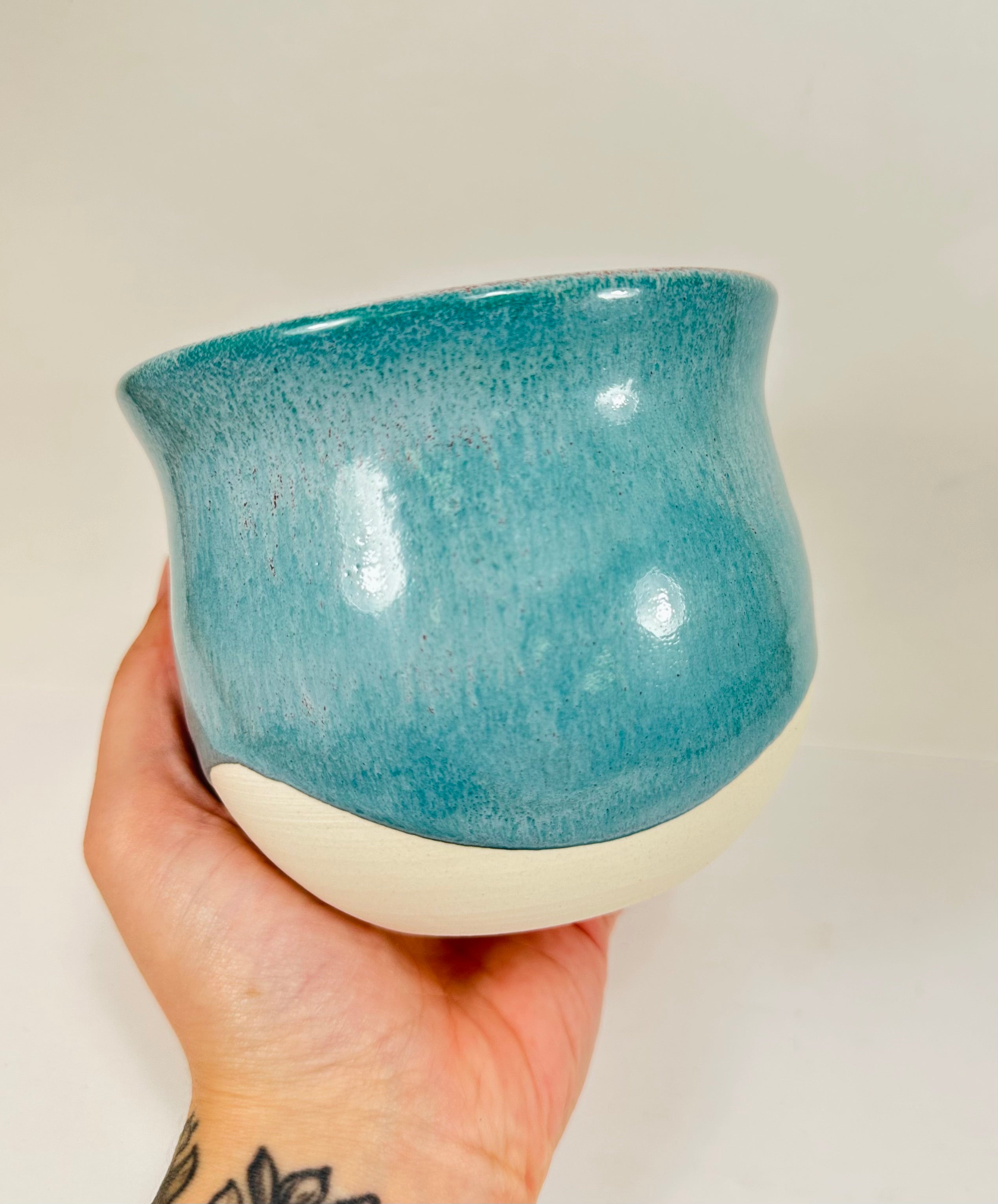 A handmade ceramic planter. The planter is glazed in a beautiful turquoise and cream colour. The planter is round in shape with a wide flared rim. The planter is left unglazed on the inside and on the bottom quarter of the pot.