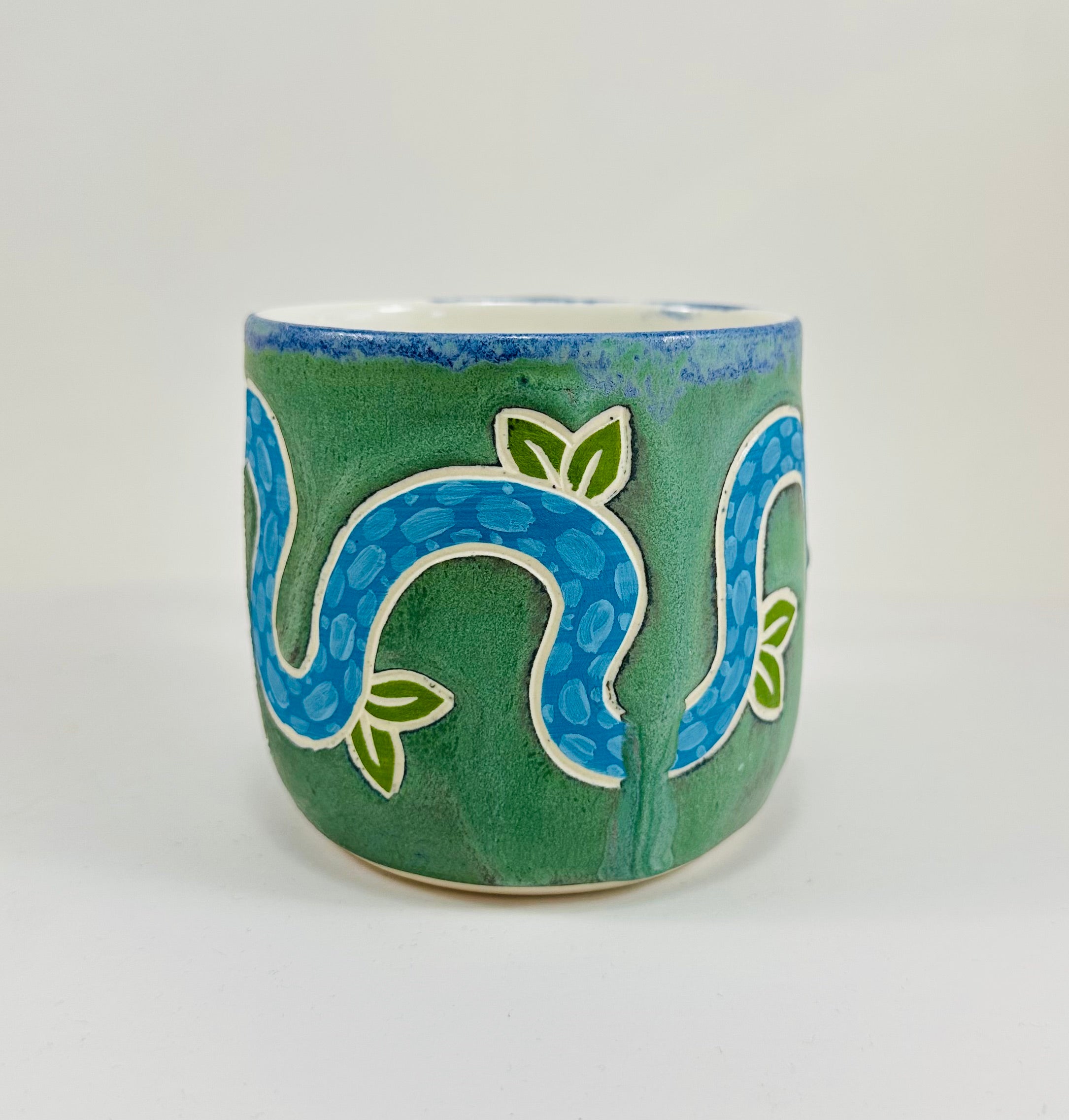 A handmade ceramic mug with a blue snake illustration on it. The mug is glazed in a beautiful robins egg green on the outside and white on the inside. The mug is made from porcelain and has a smooth comfortable handle.