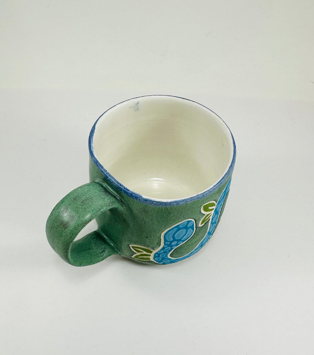 A handmade ceramic mug with a blue snake illustration on it. The mug is glazed in a beautiful robins egg green on the outside and white on the inside. The mug is made from porcelain and has a smooth comfortable handle.