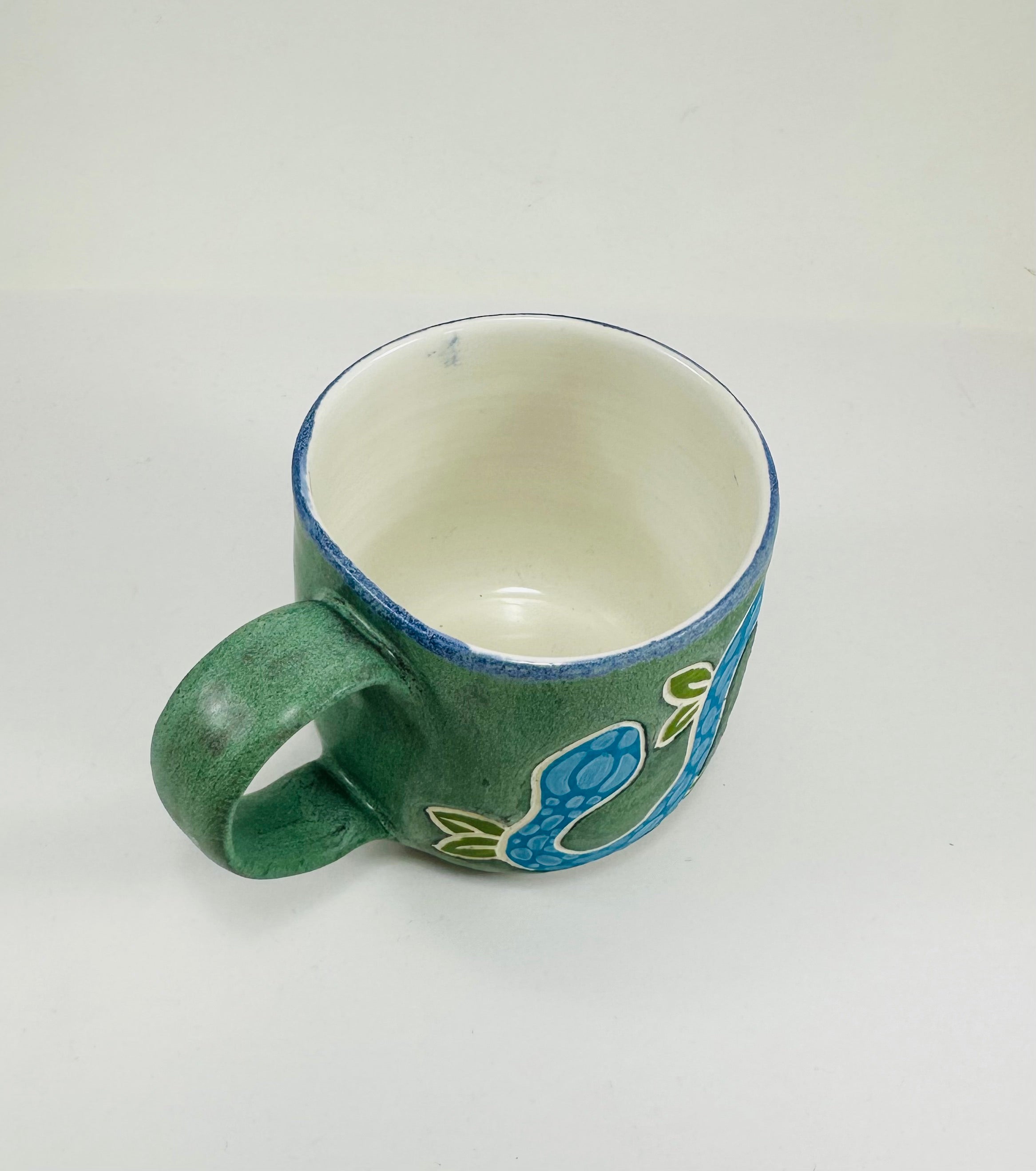 A handmade ceramic mug with a blue snake illustration on it. The mug is glazed in a beautiful robins egg green on the outside and white on the inside. The mug is made from porcelain and has a smooth comfortable handle.