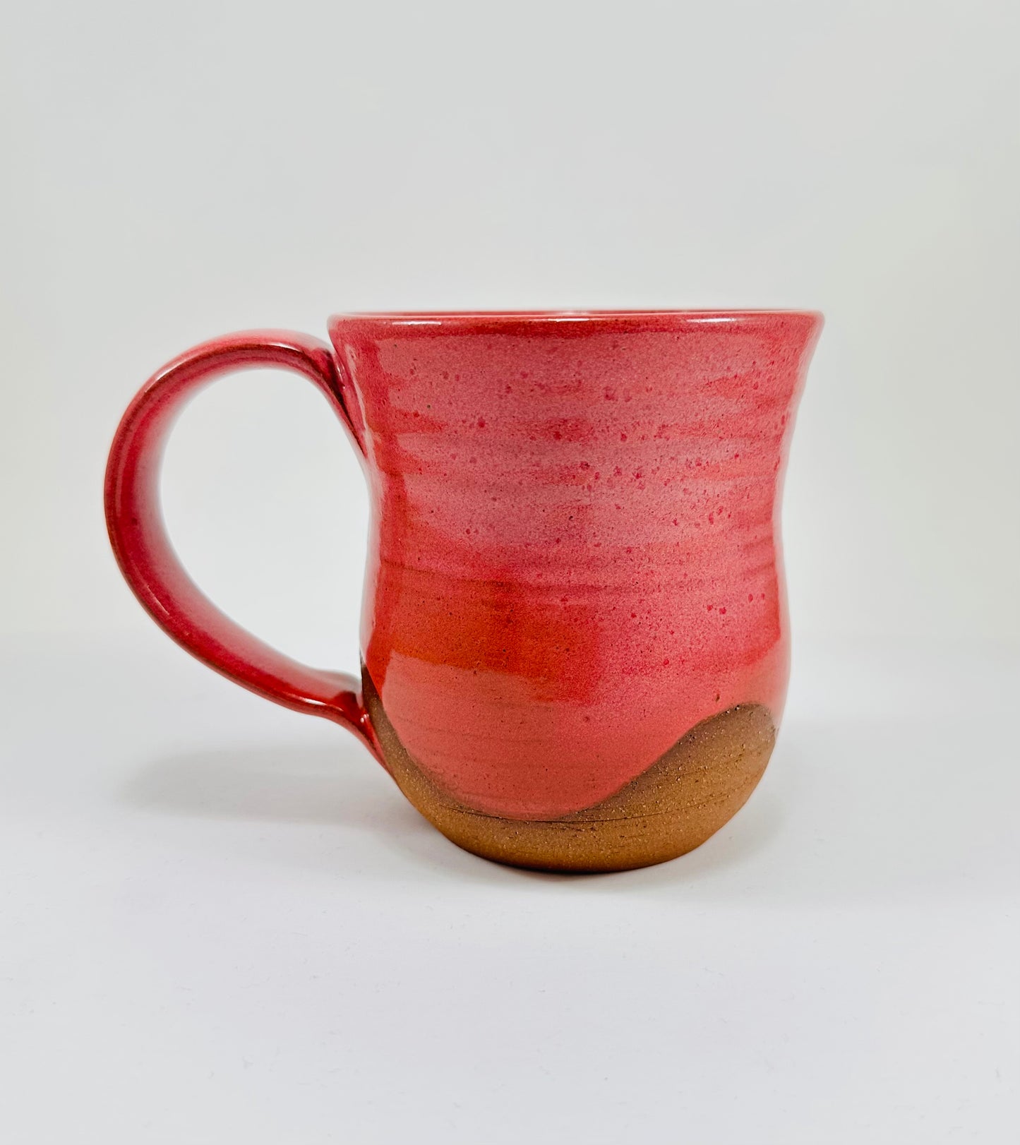 A handmade ceramic mug with a stunning pink glaze on red clay.