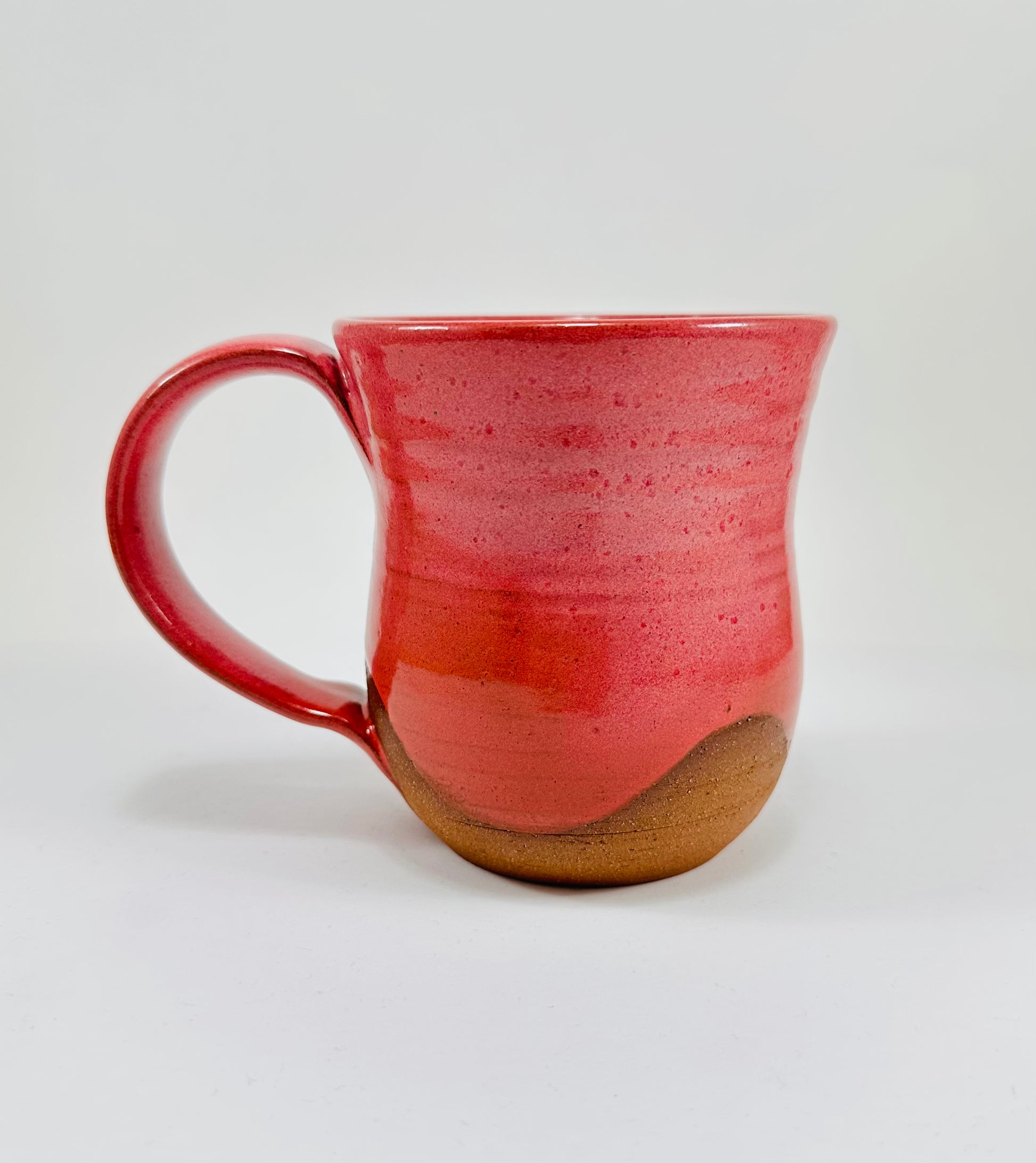 A handmade ceramic mug with a stunning pink glaze on red clay.