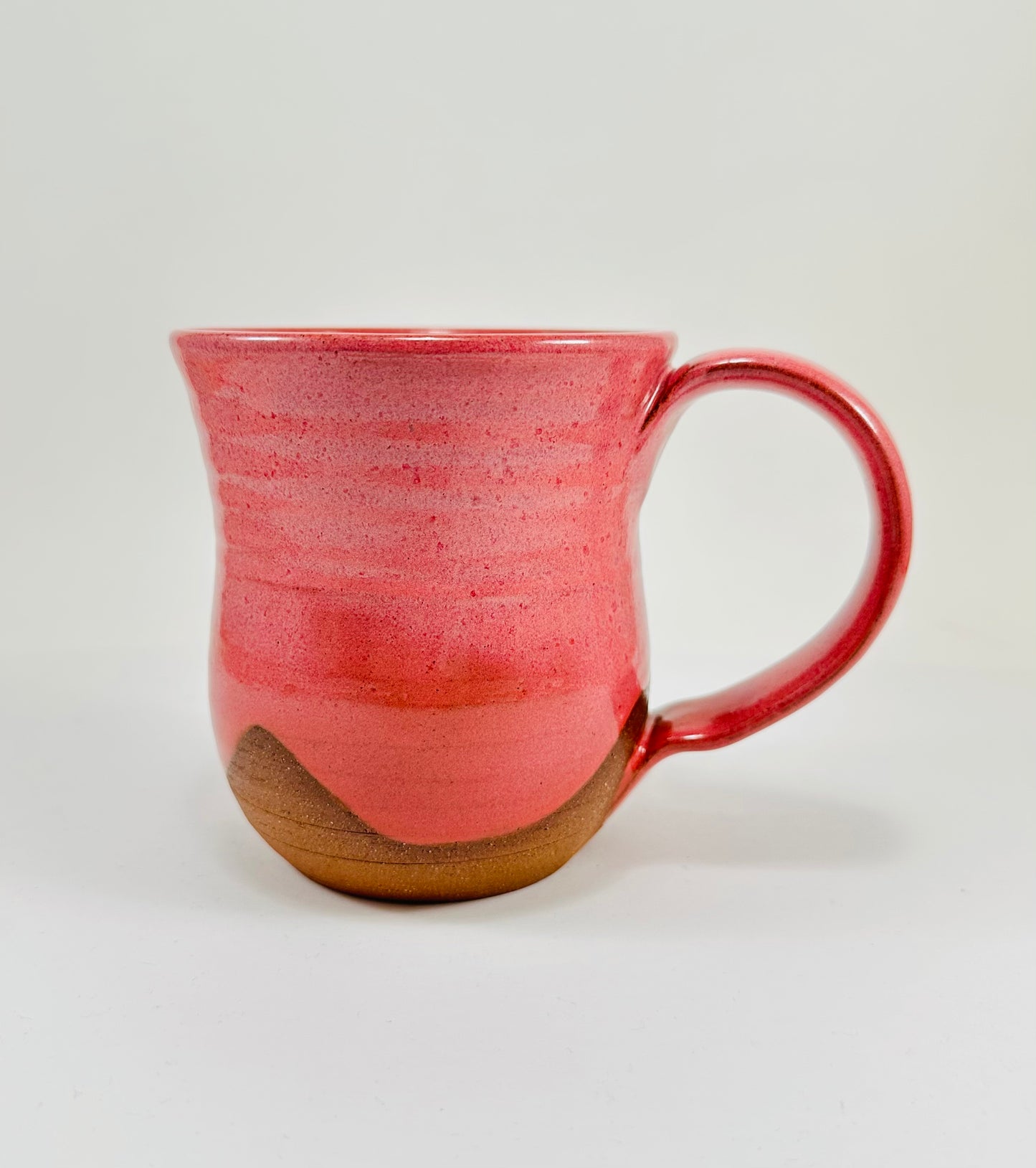 A handmade ceramic mug with a stunning pink glaze on red clay.