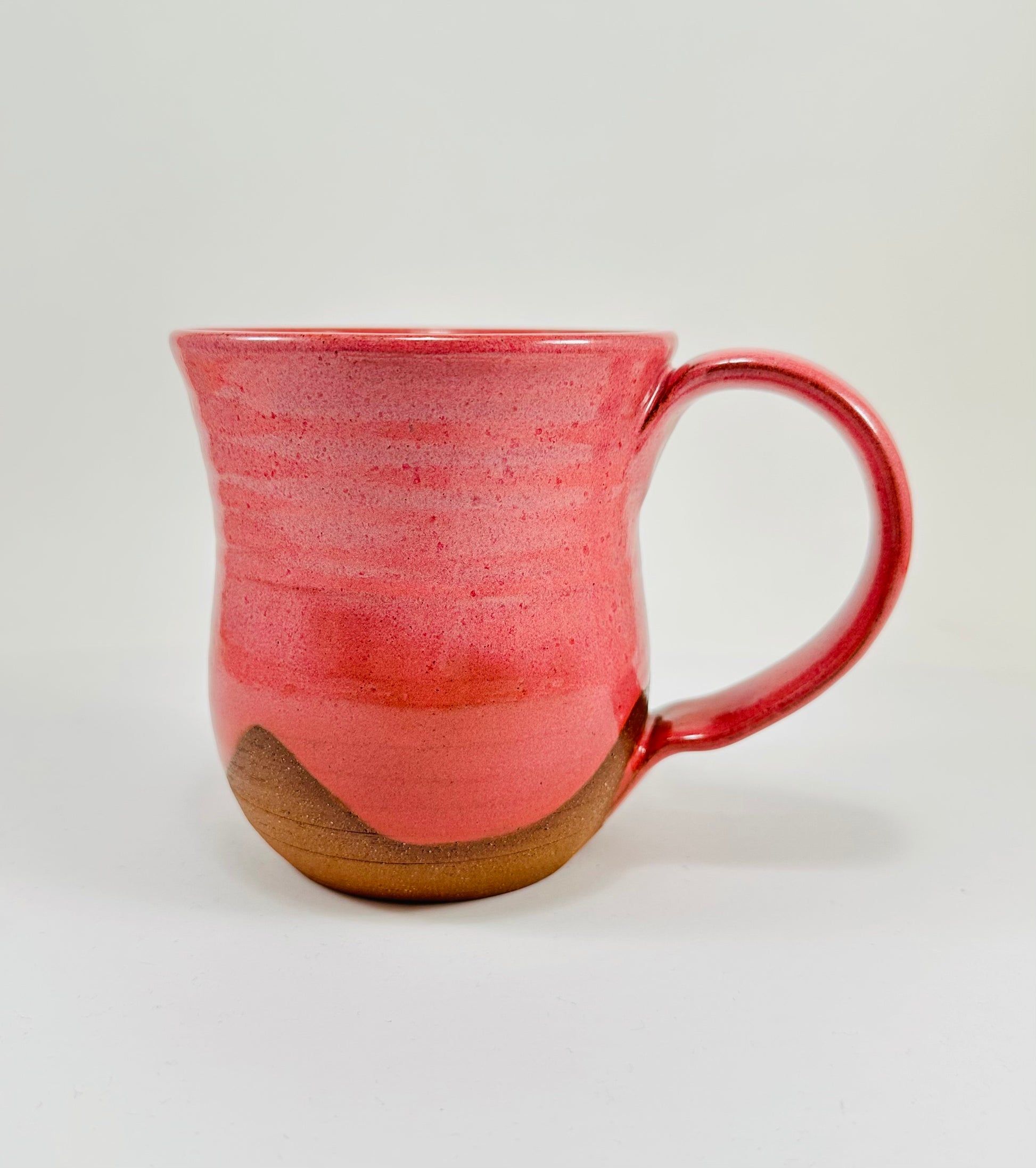 A handmade ceramic mug with a stunning pink glaze on red clay.