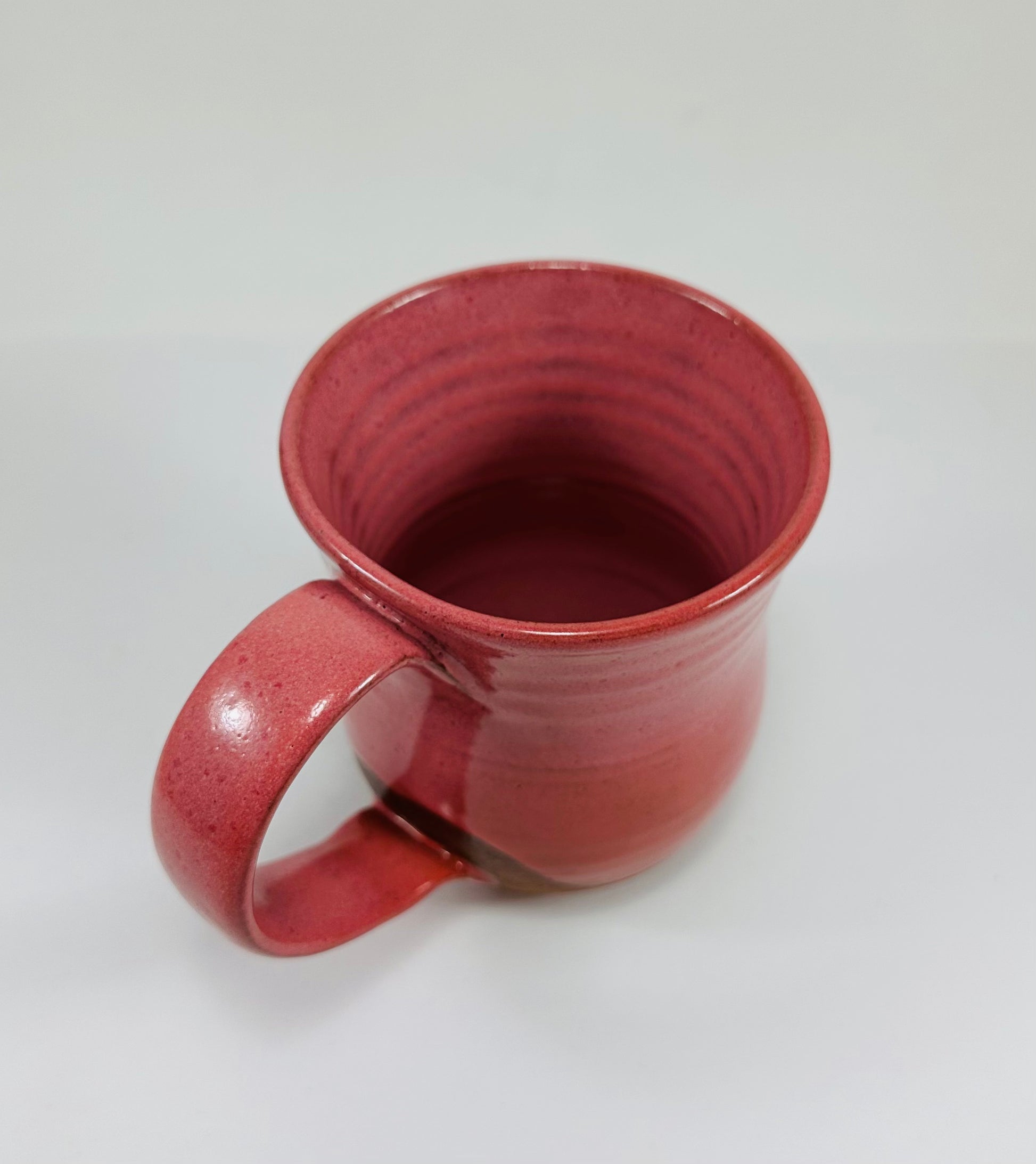 A handmade ceramic mug with a stunning pink glaze on red clay.