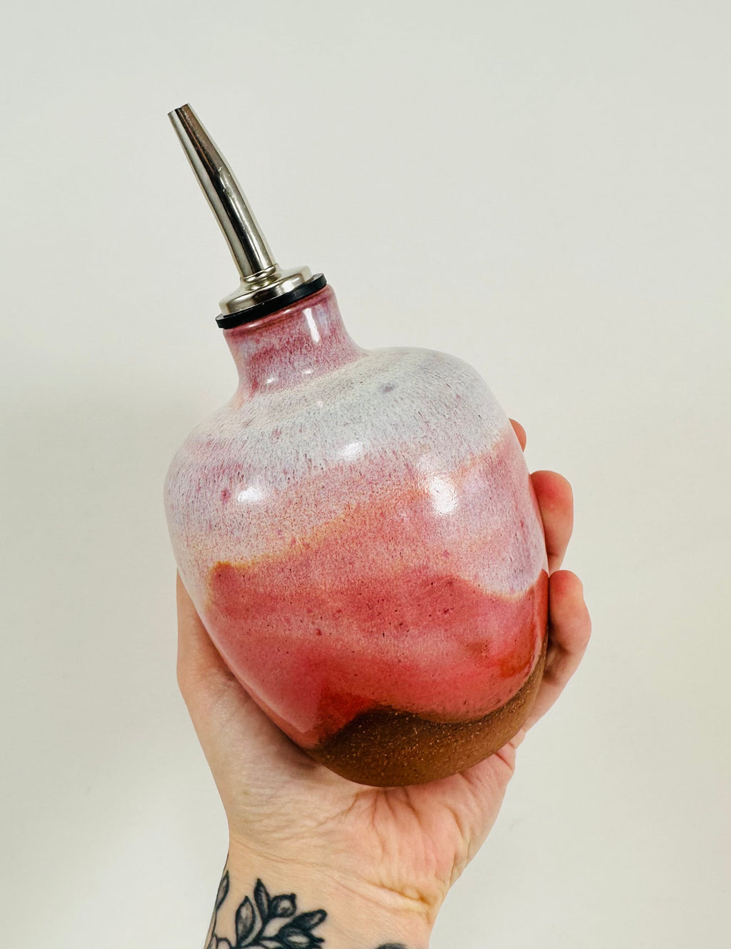 A handmade ceramic oil decanter glazed in a beautiful pink on red clay.