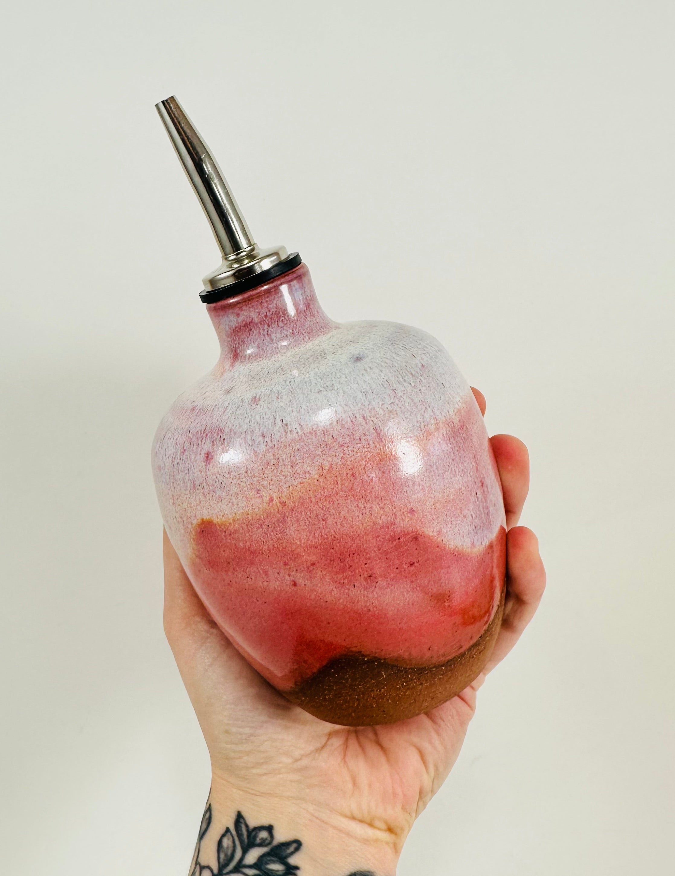 A handmade ceramic oil decanter glazed in a beautiful pink on red clay.