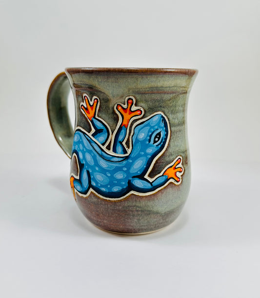 A handmade ceramic mug with a blue lizard illustration on it. The mug is made from porcelain clay and is glazed in a beautiful green glaze.