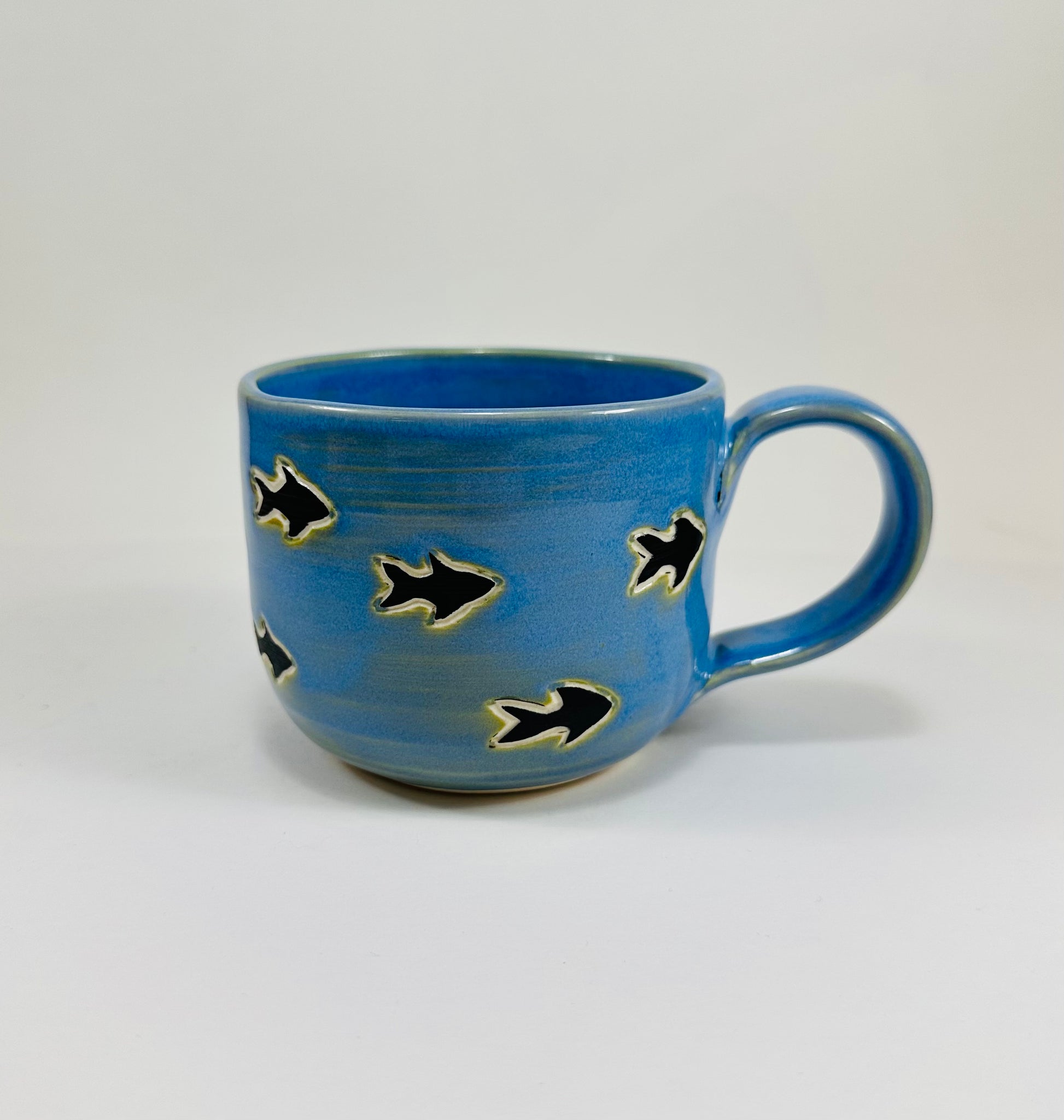 A handmade ceramic mug with an orca chasing fish illustration on it. The mug is made from porcelain clay and has a beautiful blue glaze.