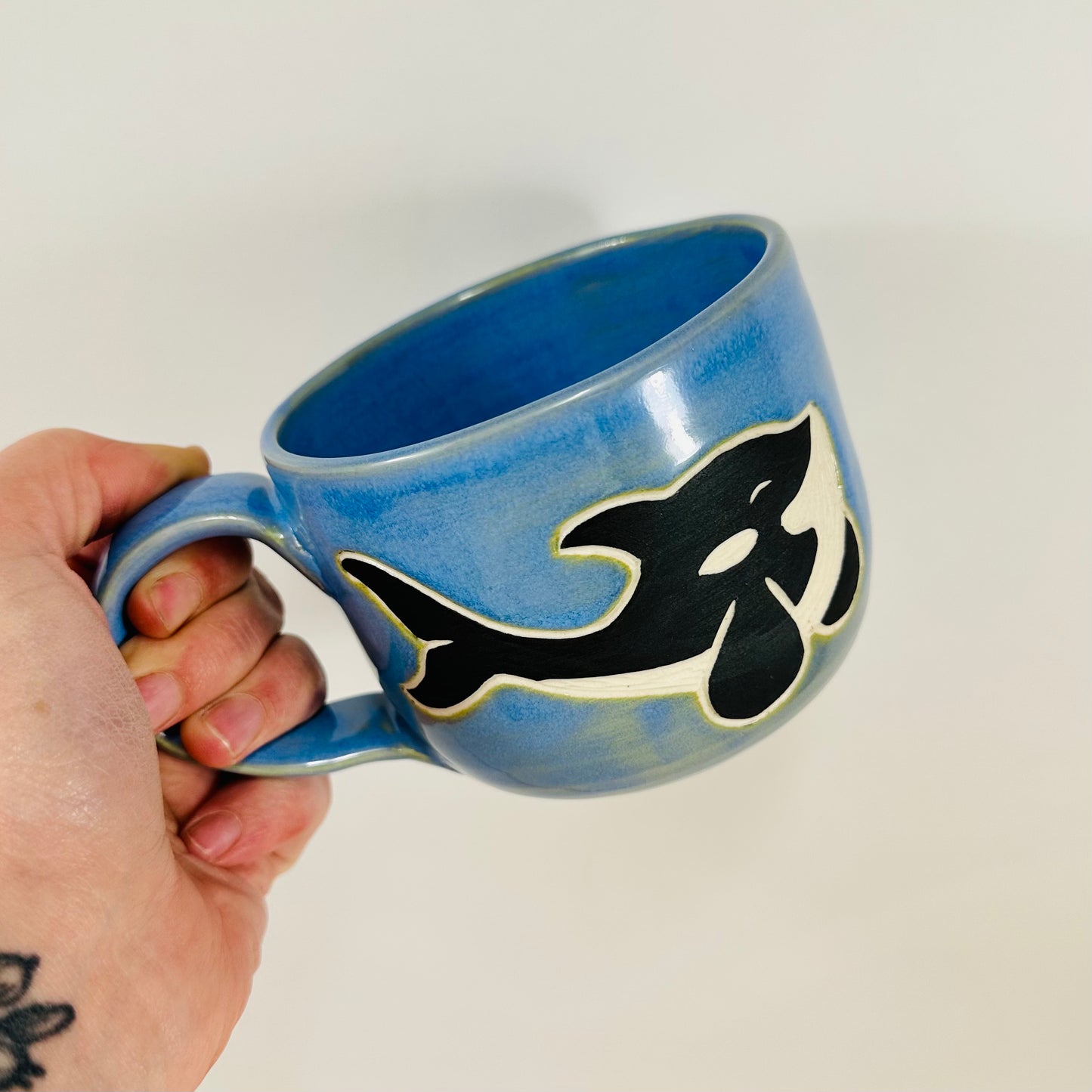 A handmade ceramic mug with an orca chasing fish illustration on it. The mug is made from porcelain clay and has a beautiful blue glaze.