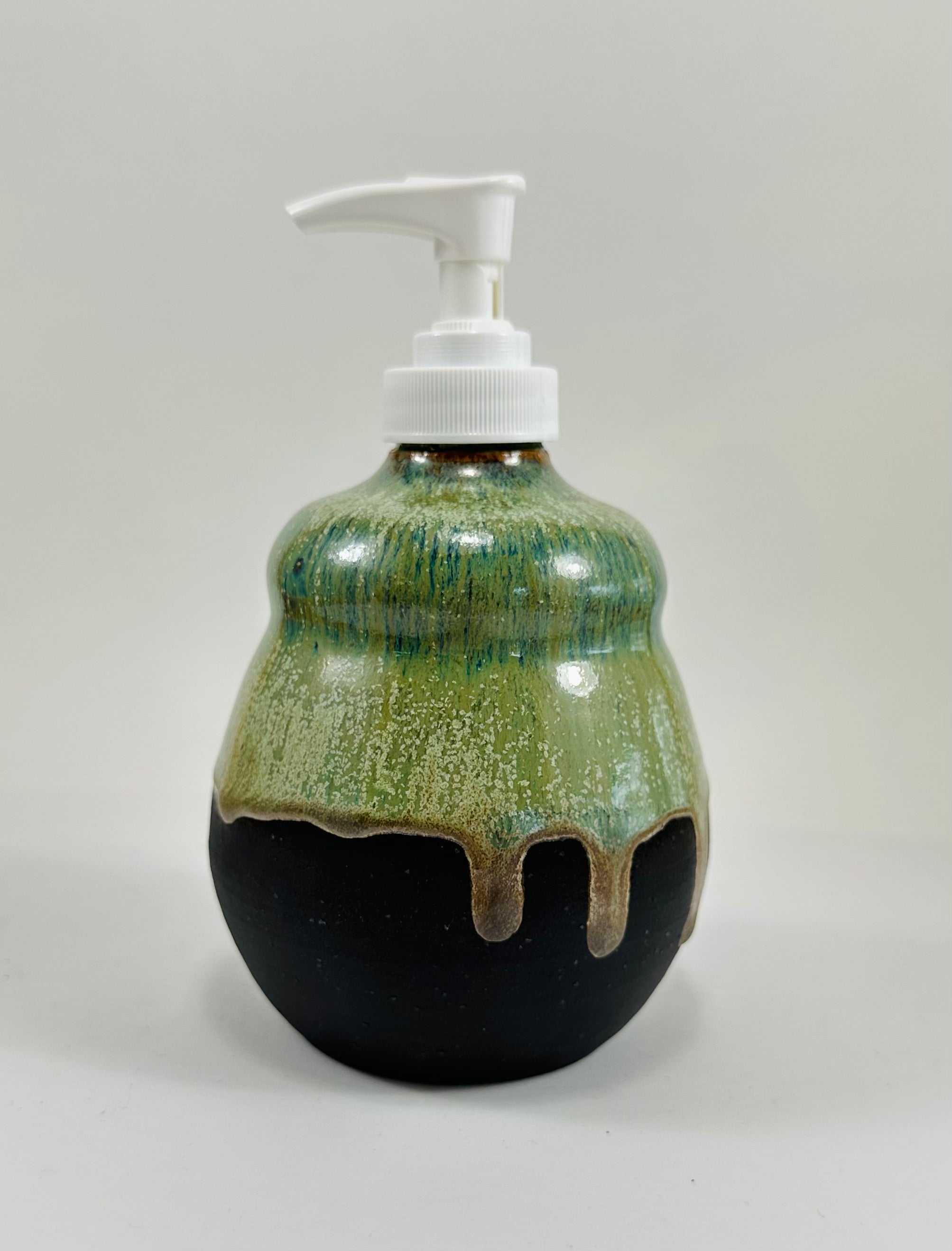 A handmade ceramic soap dispenser in a beautiful green and black glaze. The dispenser is made from porcelain clay.