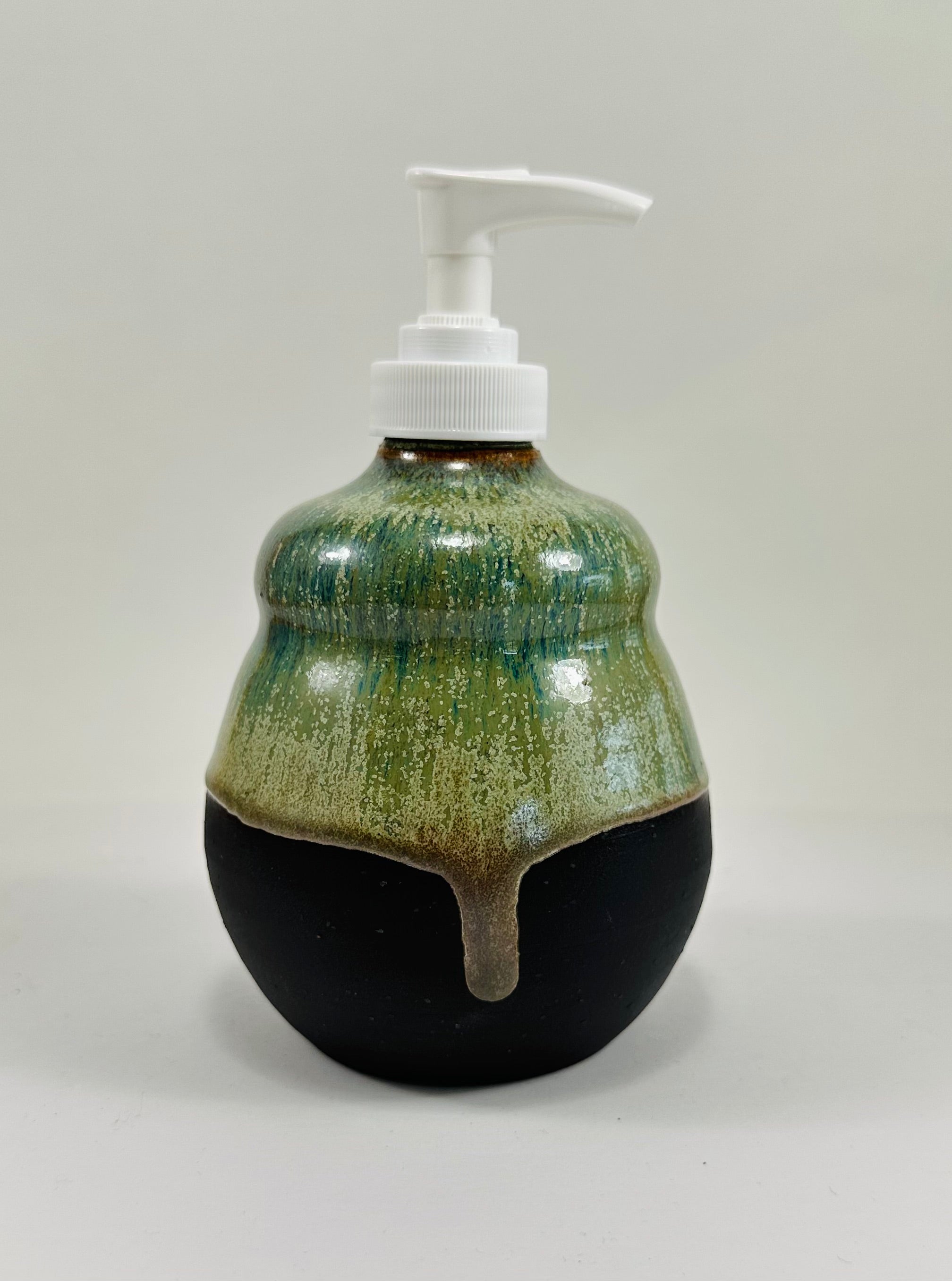 A handmade ceramic soap dispenser in a beautiful green and black glaze. The dispenser is made from porcelain clay.