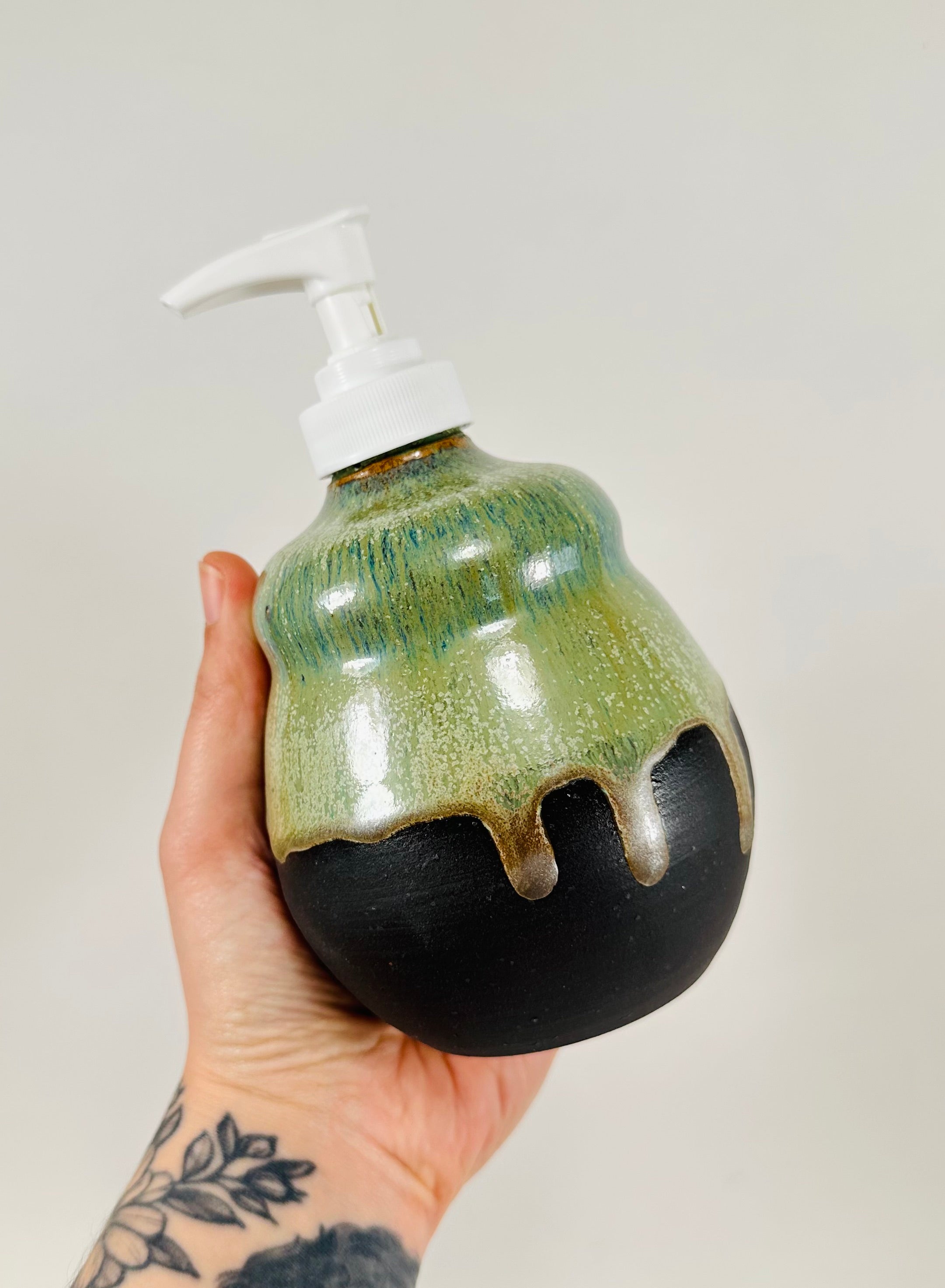 A handmade ceramic soap dispenser in a beautiful green and black glaze. The dispenser is made from porcelain clay.